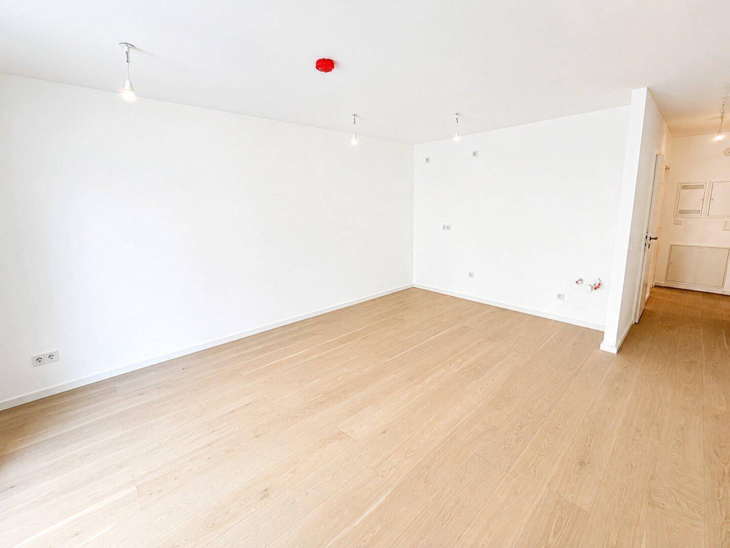 Heller, leerer Raum mit weißen Wänden und modernem Holzparkettboden.