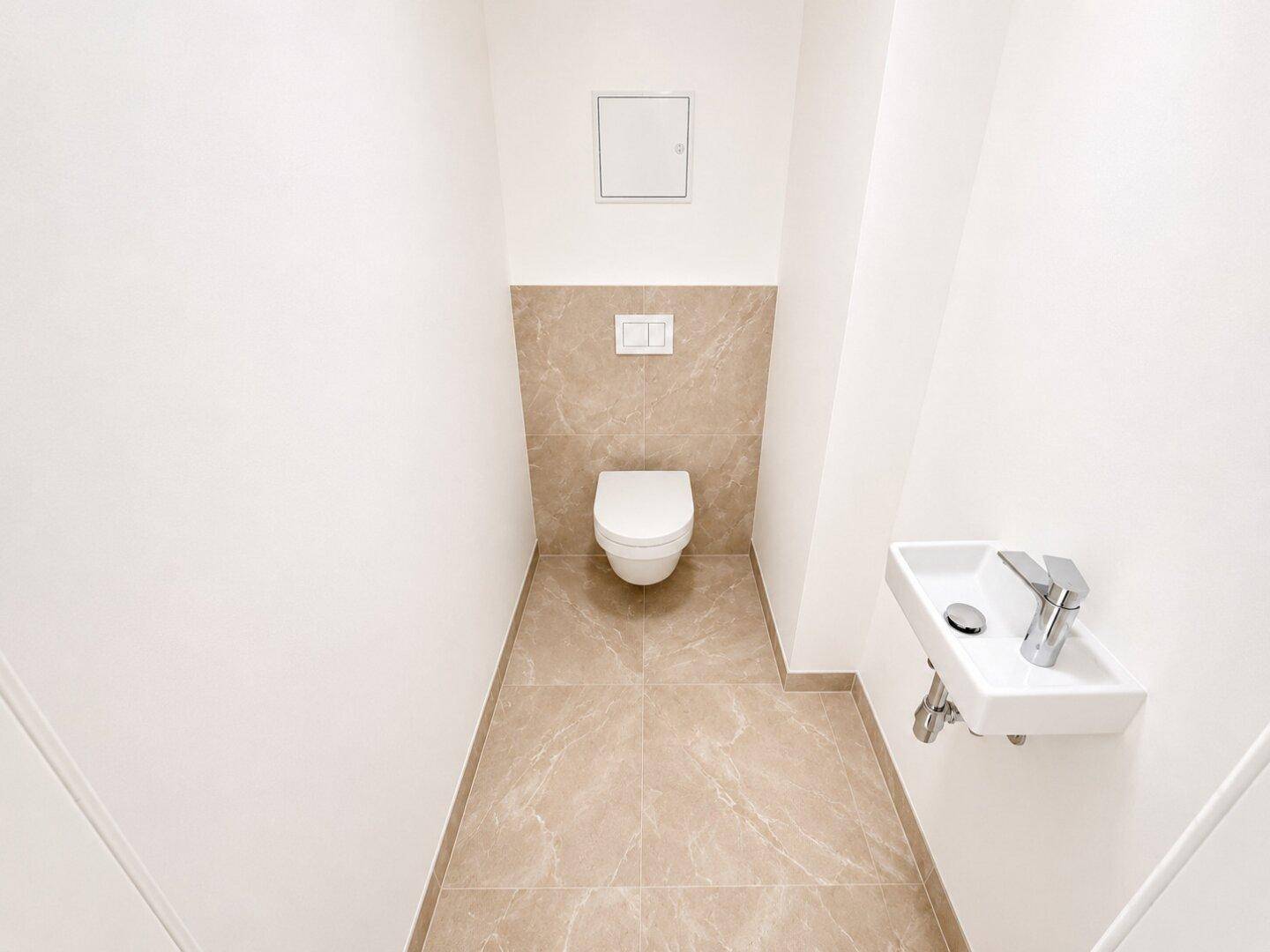 Modernes Gäste-WC mit Wand-WC, kleinem Waschbecken und beigefarbenen Fliesen.