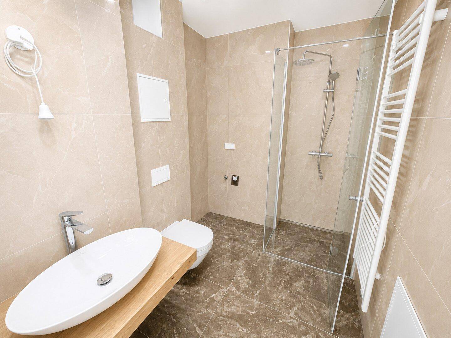 Modernes Badezimmer mit begehbarer Dusche, ovalem Waschbecken auf Holzplatte und beigefarbenen Fliesen.