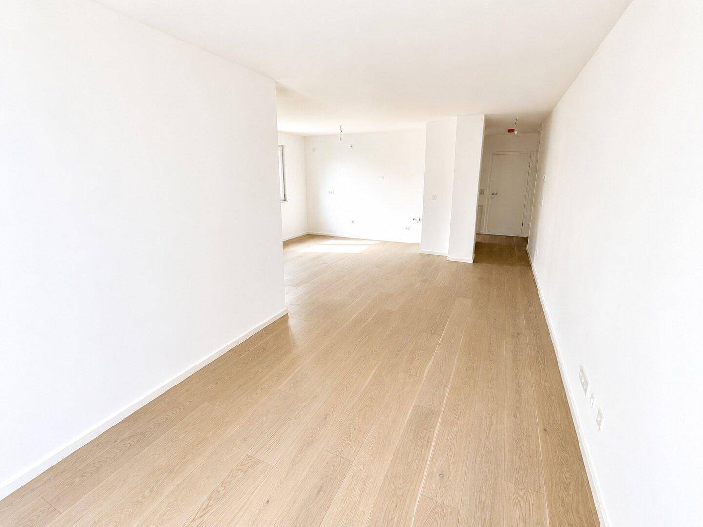 Geräumiger, heller Wohnbereich mit hellem Holzfußboden und weißen Wänden, ideal für offene Gestaltung.