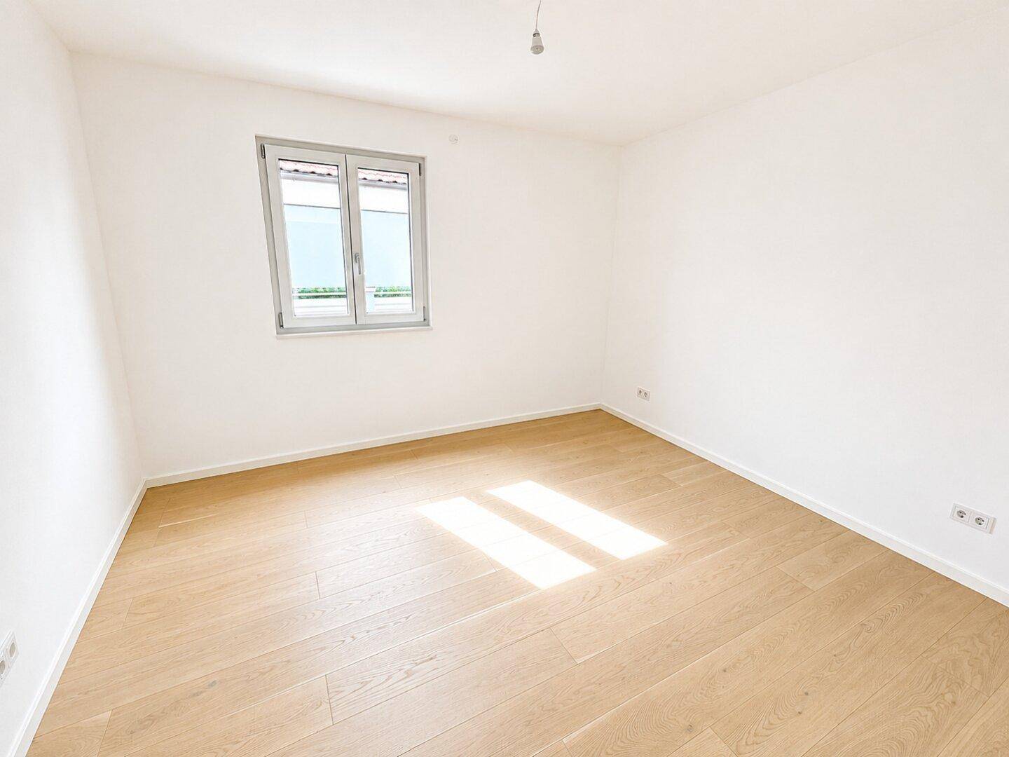 Helles Schlafzimmer mit Holzparkettboden und einem Fenster mit Rollläden, bereit zur Einrichtung.