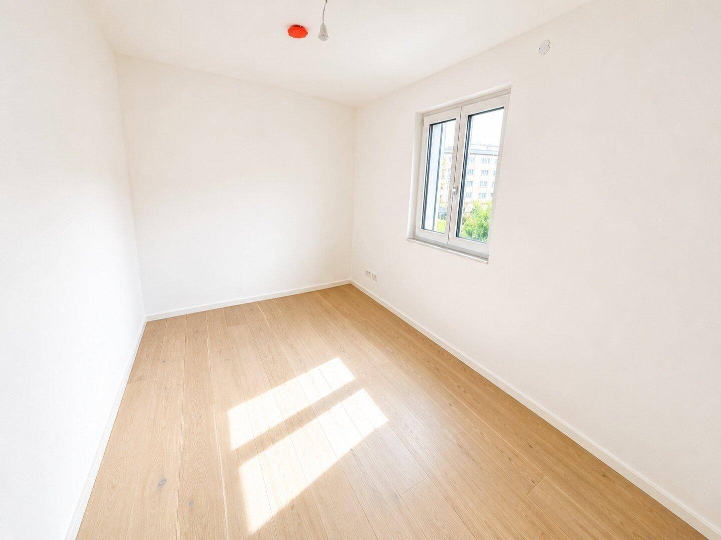 Freundliches Schlafzimmer mit hellem Holzfußboden und einem großen Fenster, das viel Tageslicht hereinlässt.