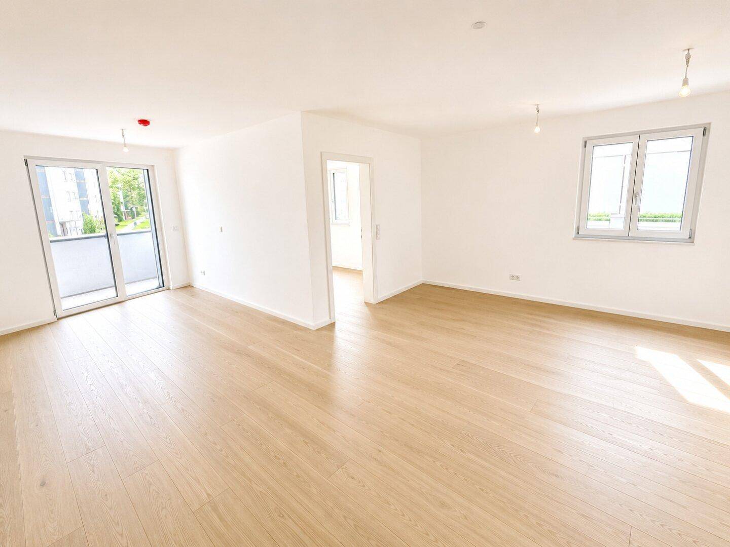 Großer, heller Wohnbereich mit Zugang zum Balkon und hellem Holzparkettboden, ideal für Familien.