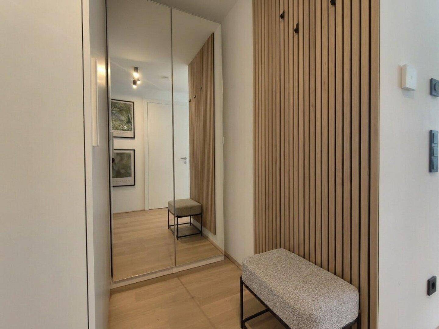 Moderner Eingangsbereich mit Holzlamellenwand, Sitzbank und großen Spiegelschränken.