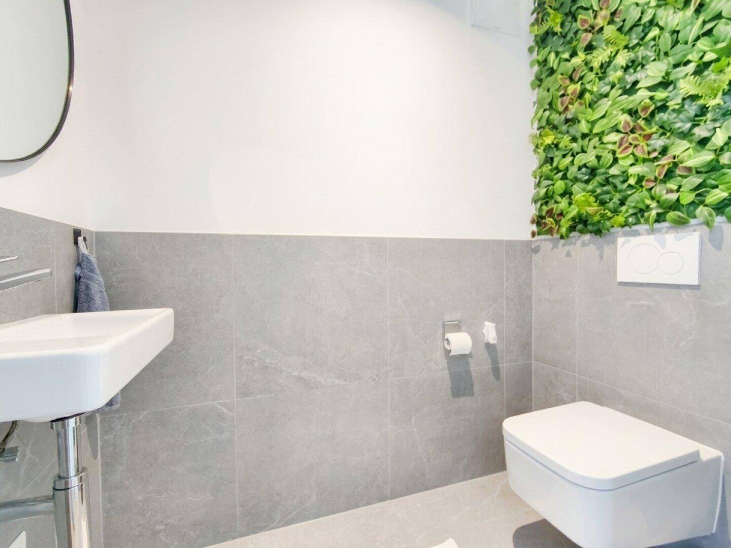 Modernes Gäste-WC mit grauen Fliesen, wandhängendem WC und dekorativer Pflanzenwand.