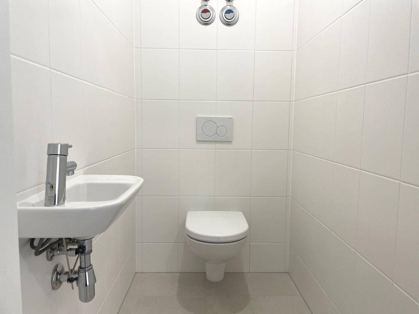Modernes Gäste-WC mit weißen Fliesen, wandhängendem WC und kleinem Handwaschbecken.