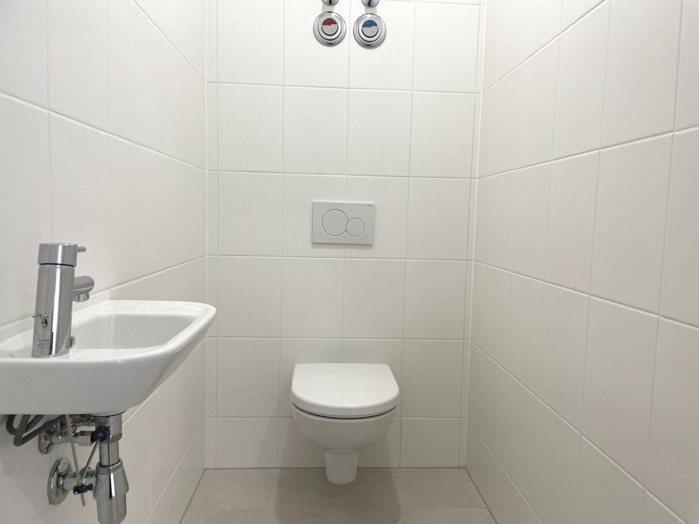 Helles Gäste-WC mit weißen Wandfliesen, wandhängender Toilette und kompaktem Waschbecken.