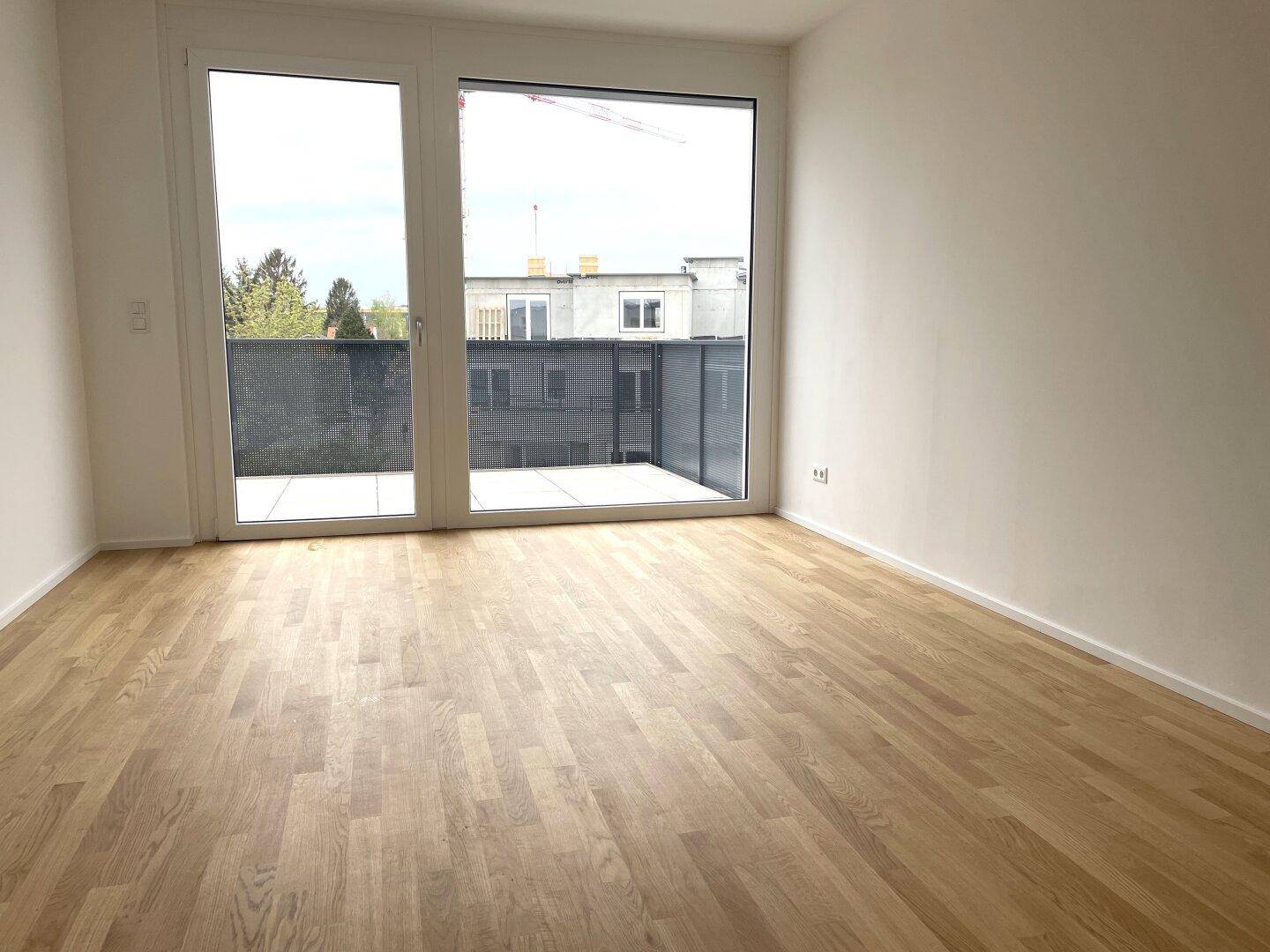 Lichtdurchfluteter Raum mit Holzboden und Zugang zu einem Balkon, ideal für Wohn- oder Schlafzimmer.