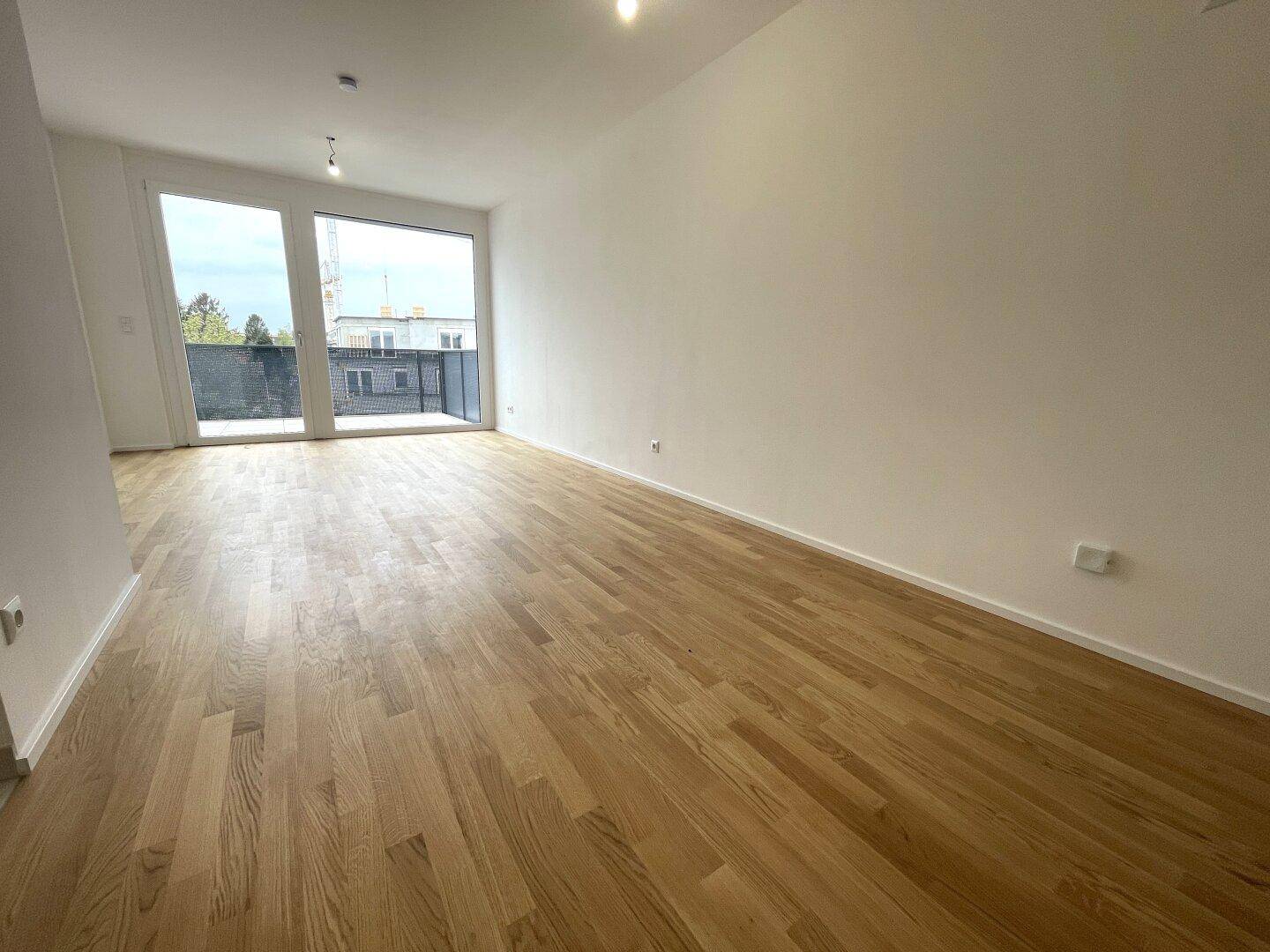 Geräumiger, heller Wohnbereich mit Holzboden und großem Fenster mit Zugang zum Außenbereich.