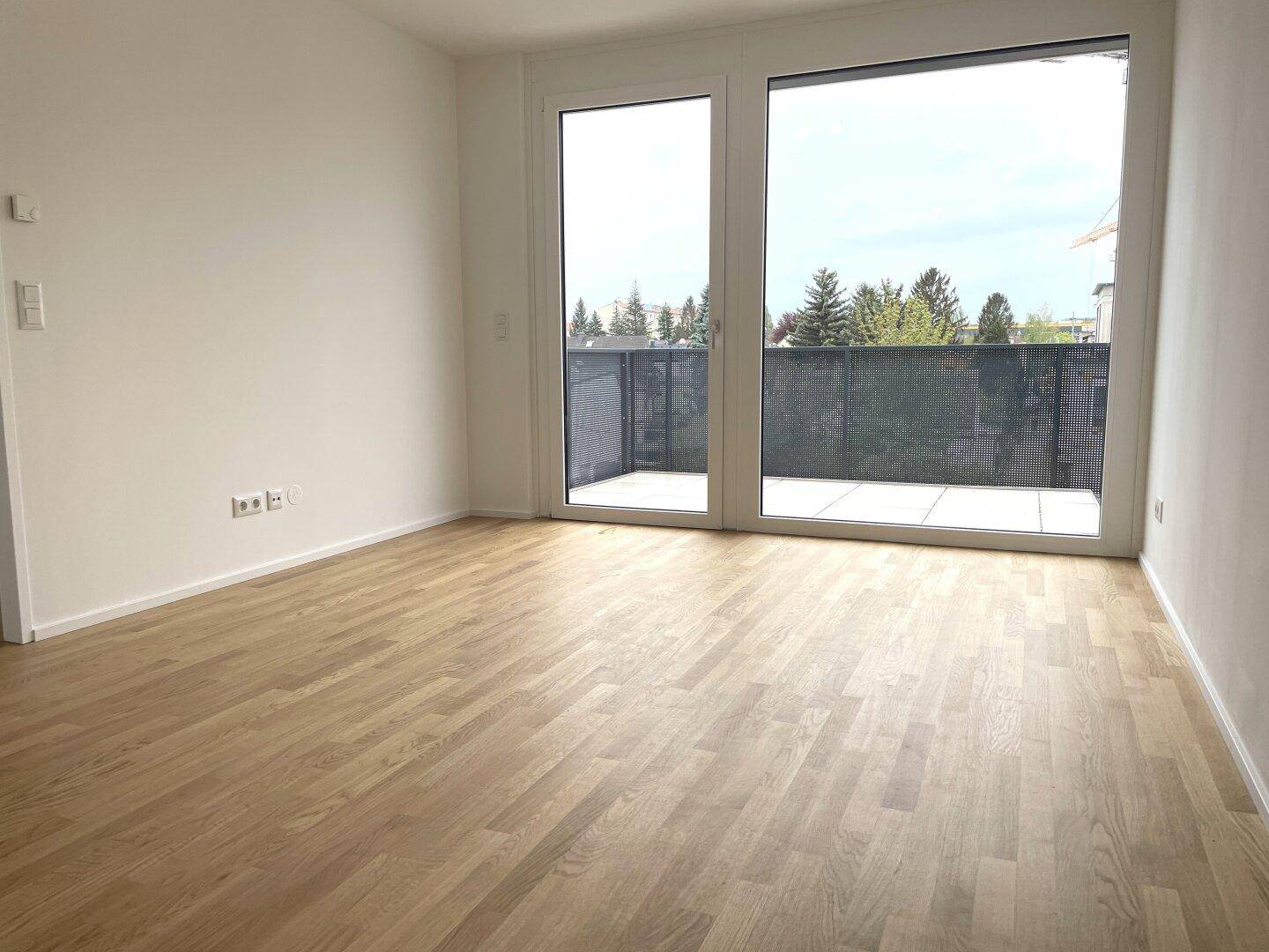 Heller Raum mit Holzboden und breiter Fensterfront, die einen Blick ins Grüne bietet.