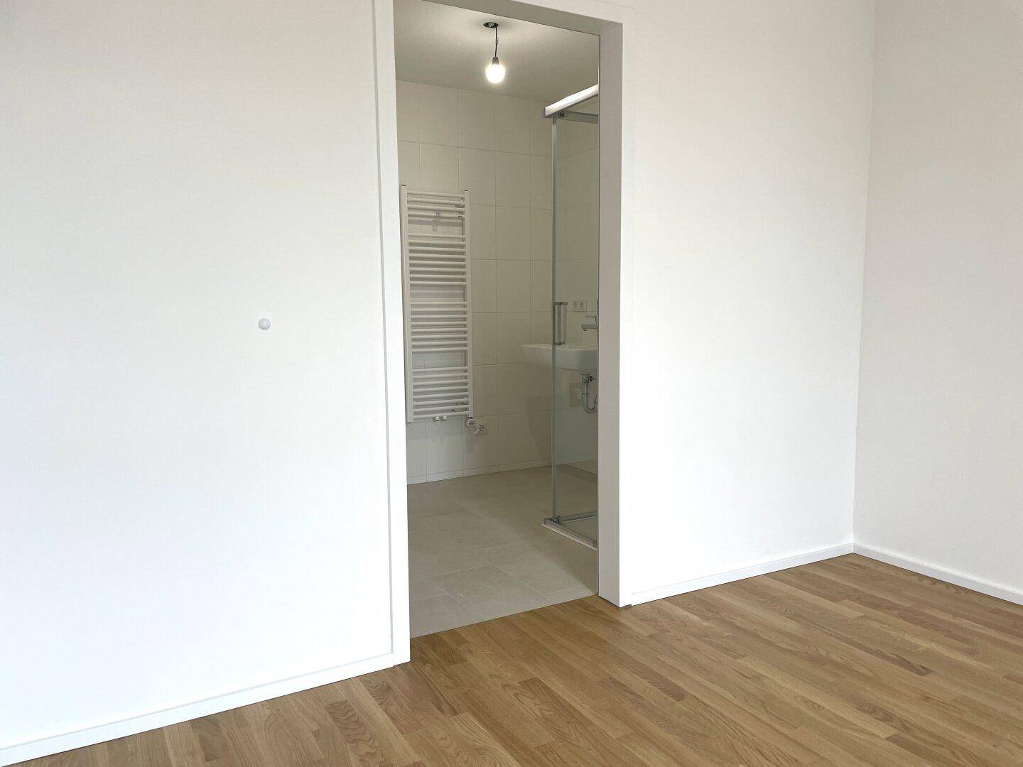 Schlafzimmer mit Holzboden und direktem Zugang zu einem modernen Badezimmer mit Dusche.