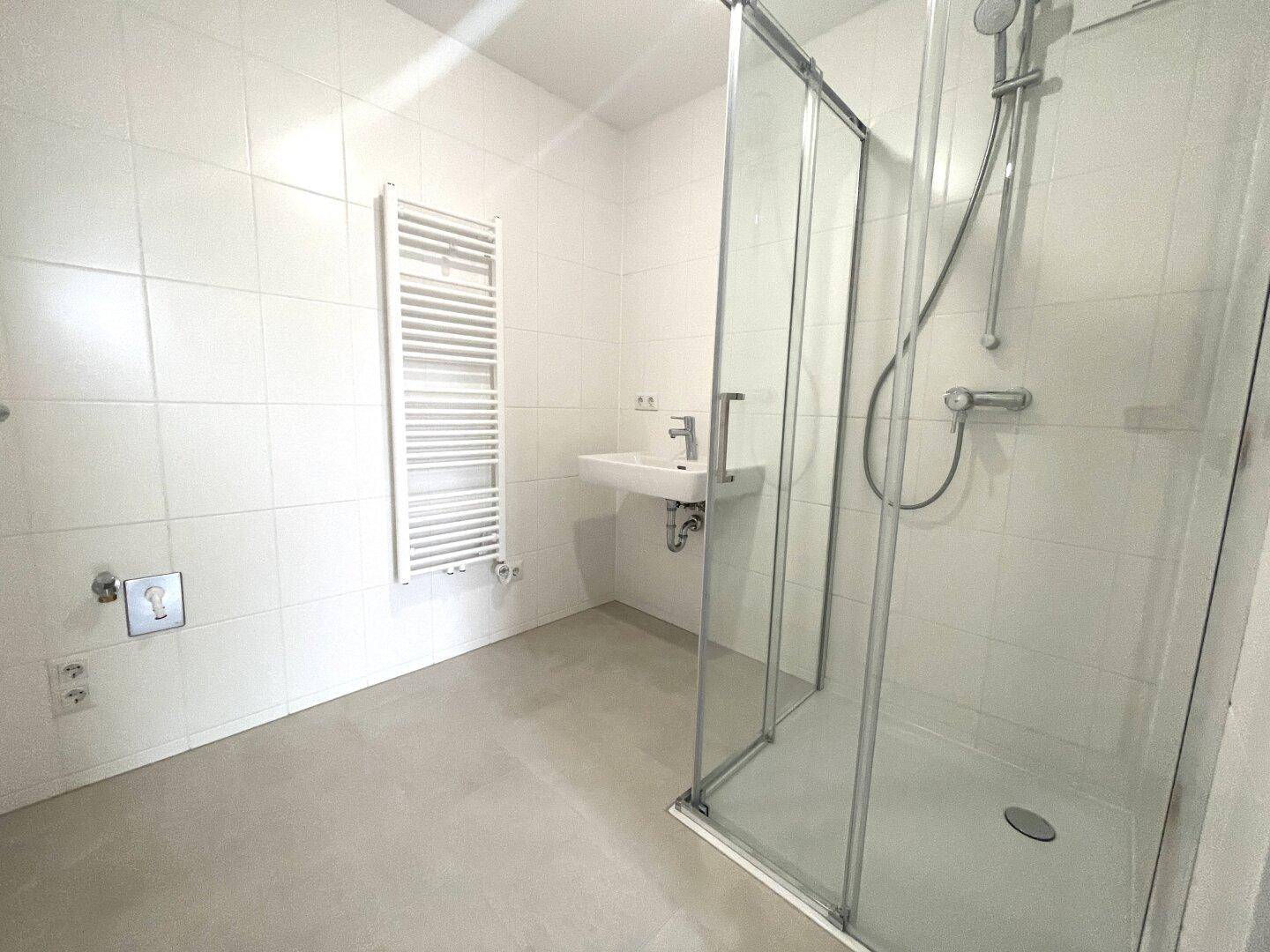 Modernes Badezimmer mit weißen Fliesen, Duschkabine, Waschbecken und beheiztem Handtuchhalter.