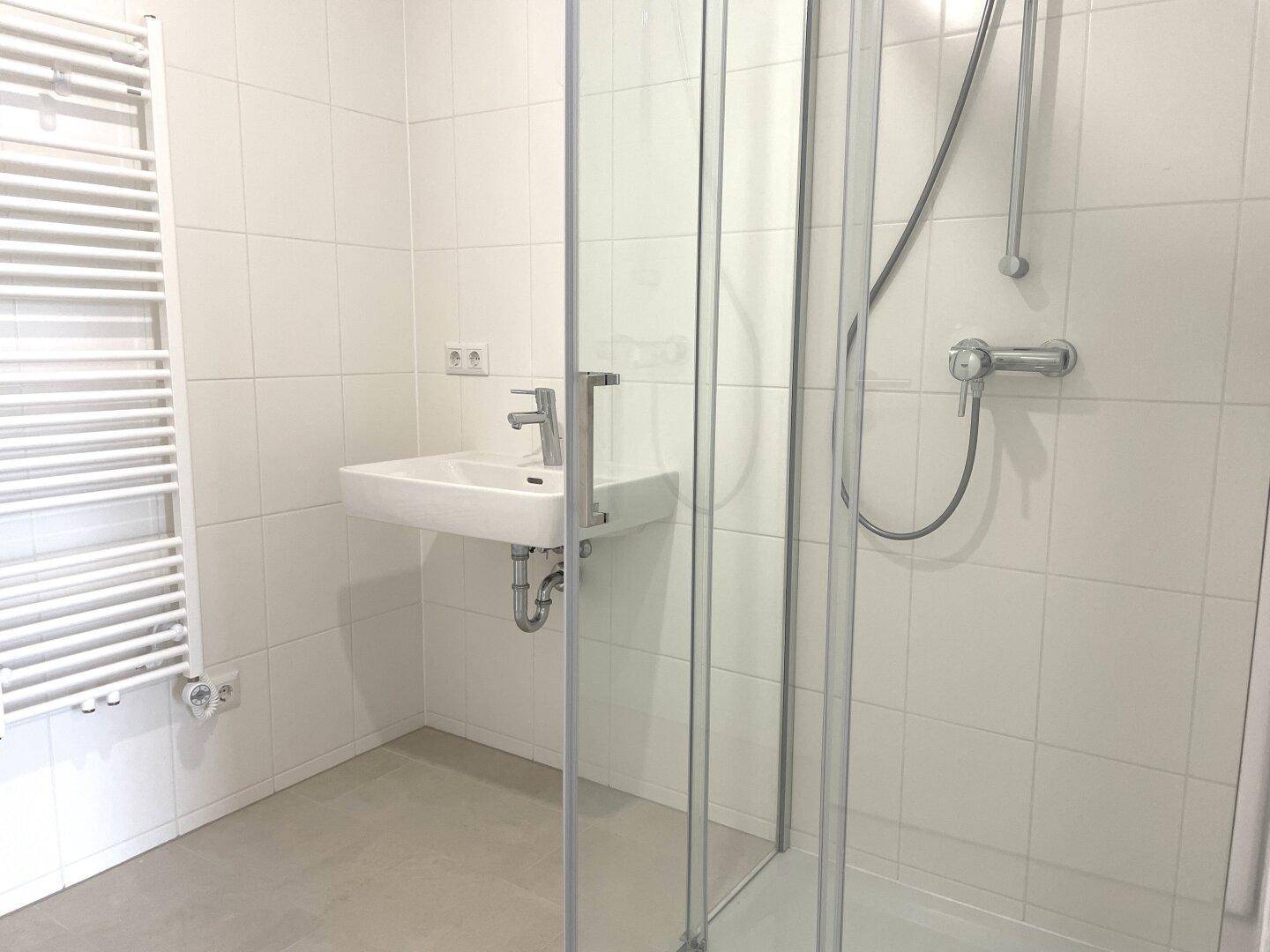 Detailansicht des modernen Waschbeckens und der Duschkabine in einem hell gefliesten Badezimmer.