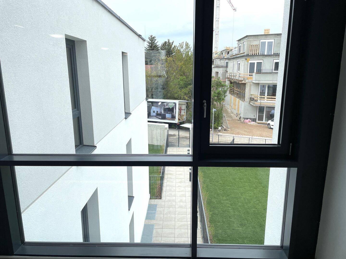 Blick aus dem Fenster auf die moderne Gebäudefassade und eine gepflegte Grünfläche.