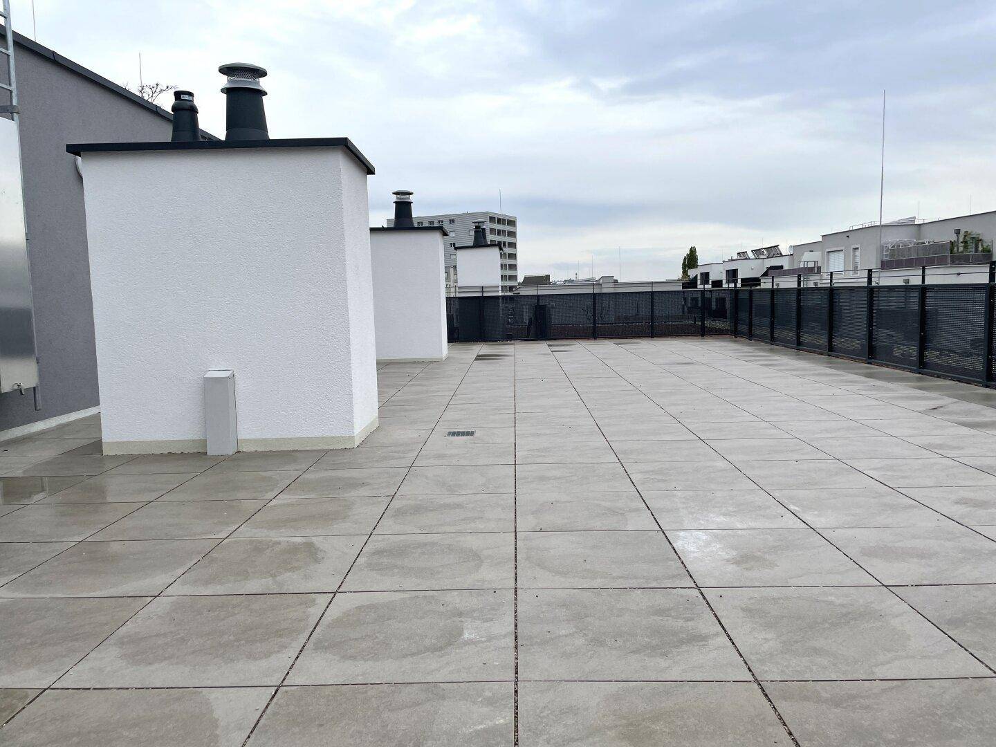 Große, geflieste Dachterrasse mit Blick auf die umliegenden Gebäude unter bewölktem Himmel.
