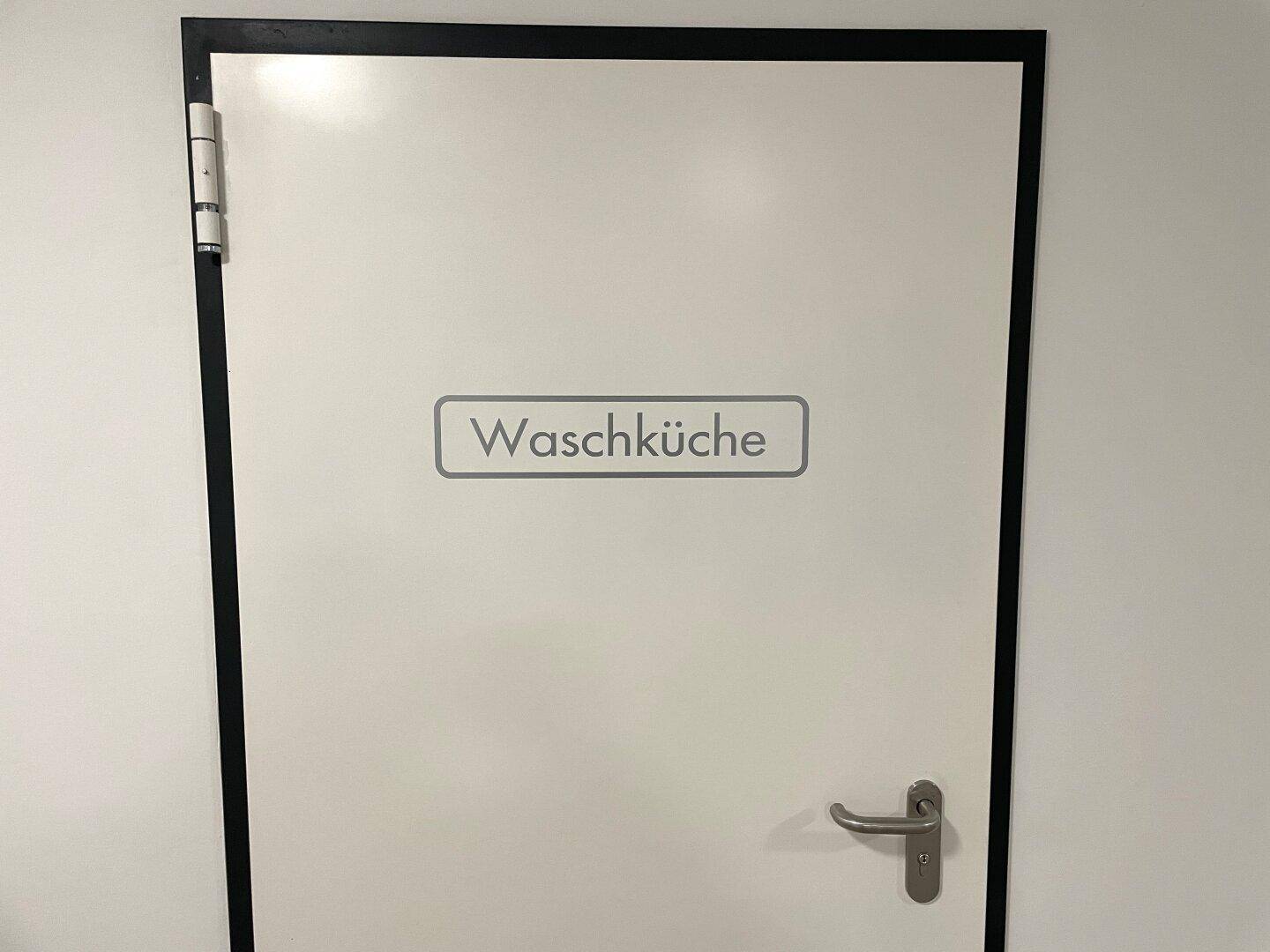 Eine weiße Tür mit der Aufschrift "Waschküche" in einem modernen Gebäude.