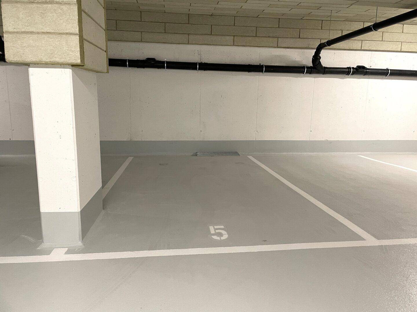 Ein leerer Parkplatz Nummer 5 in einer hellen Tiefgarage mit sauberem Boden.
