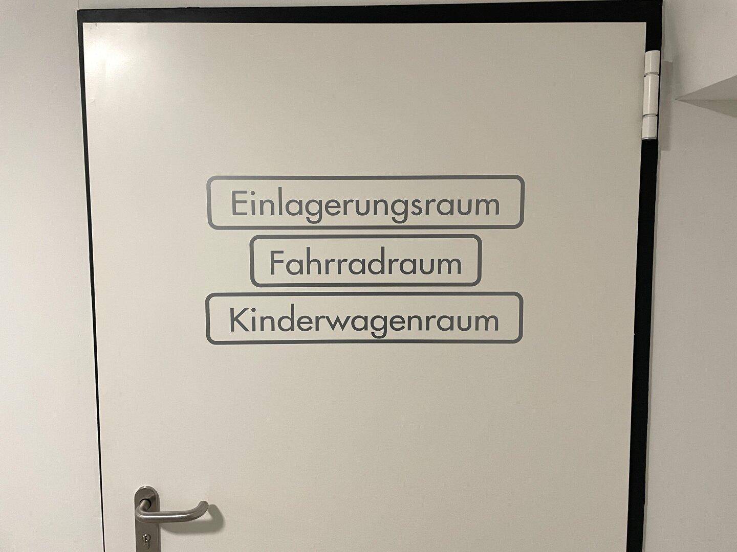 Eine weiße Tür mit Beschriftungen für Einlagerungsraum, Fahrradraum und Kinderwagenraum.