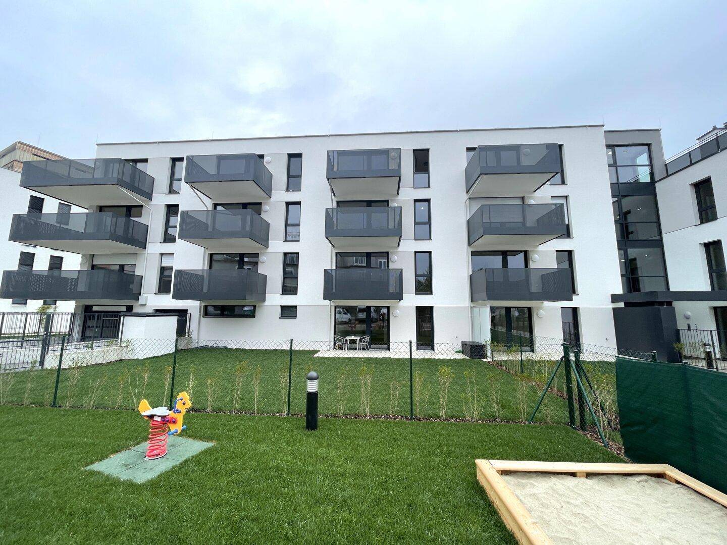 Moderne Wohnanlage mit Balkonen und einem kleinen Spielplatz im grünen Vorgartenbereich.