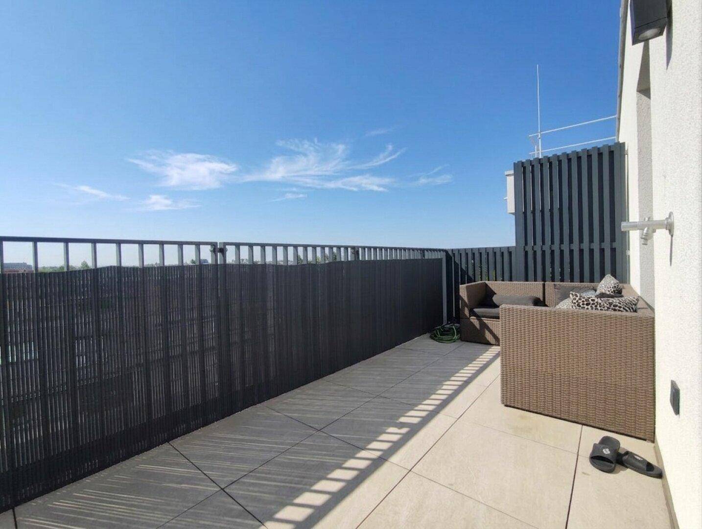 Sonnige Dachterrasse mit modernen Fliesen, Sichtschutz und bequemen Outdoor-Möbeln zum Entspannen.