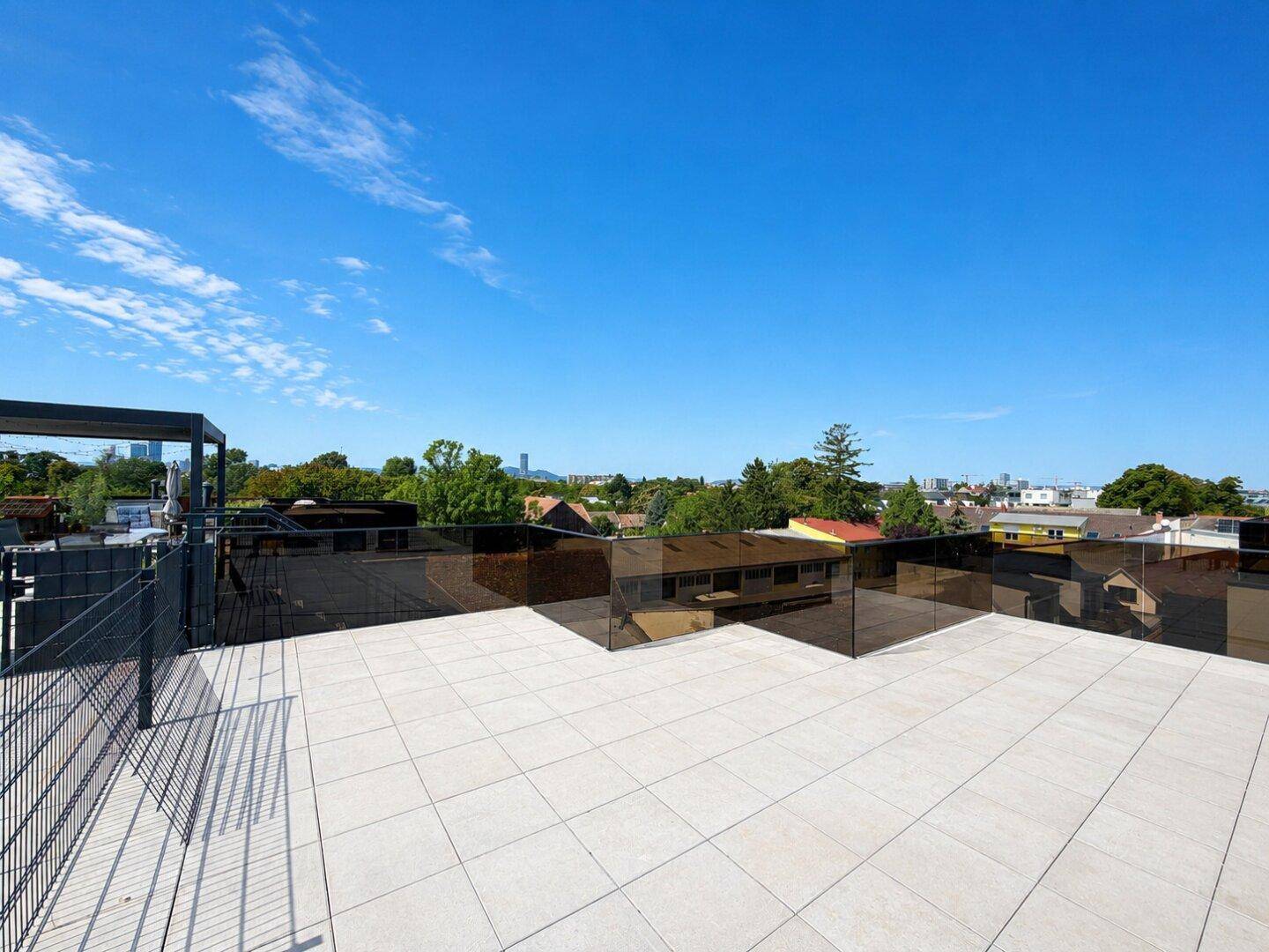 Weitläufige Dachterrasse mit moderner Glasbrüstung und Panoramablick auf die Stadt.
