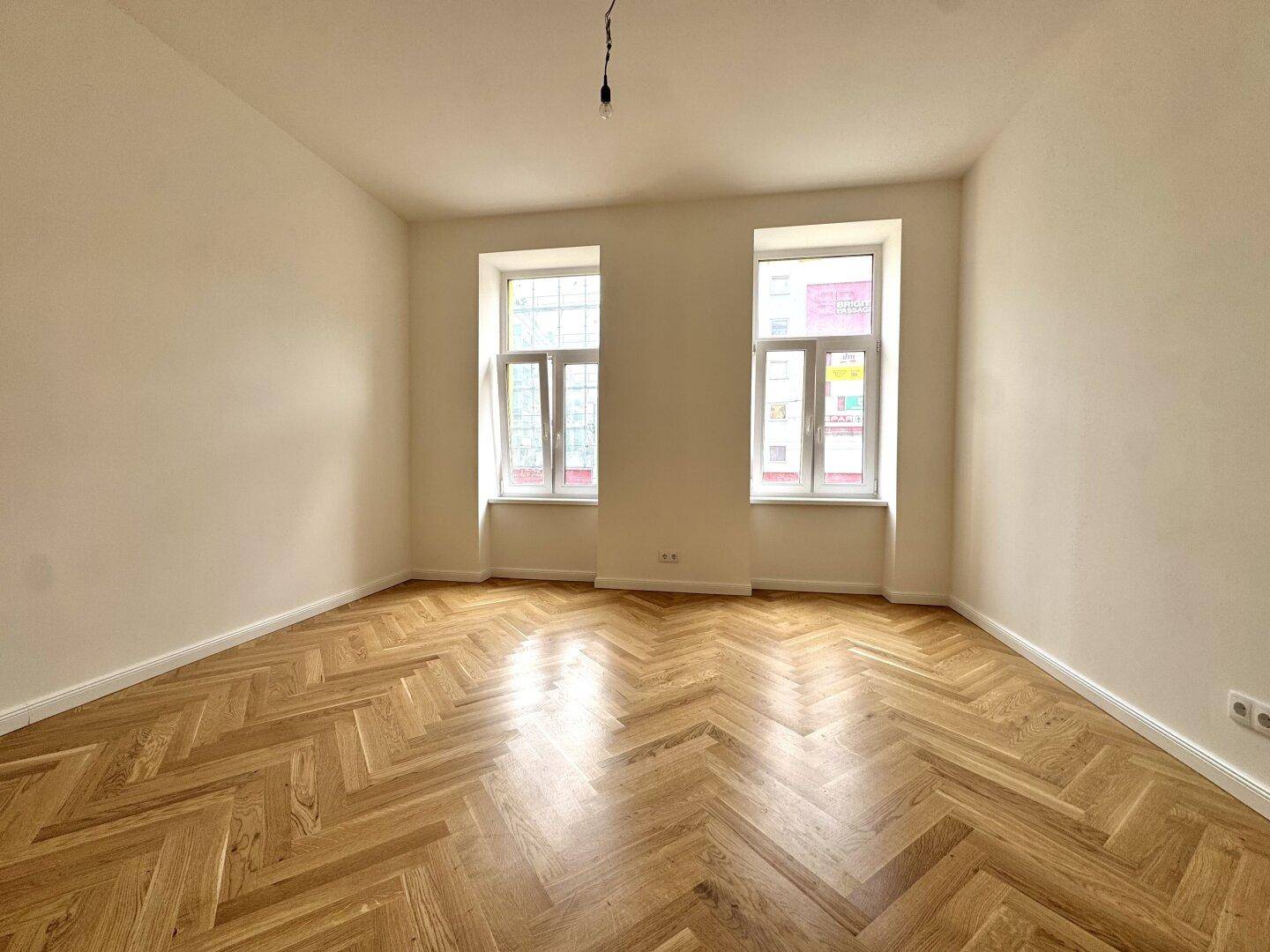 Lichtdurchfluteter Raum mit elegantem Fischgrätparkett und weiß gestrichenen Wänden, bietet vielseitige Nutzungsmöglichkeiten.