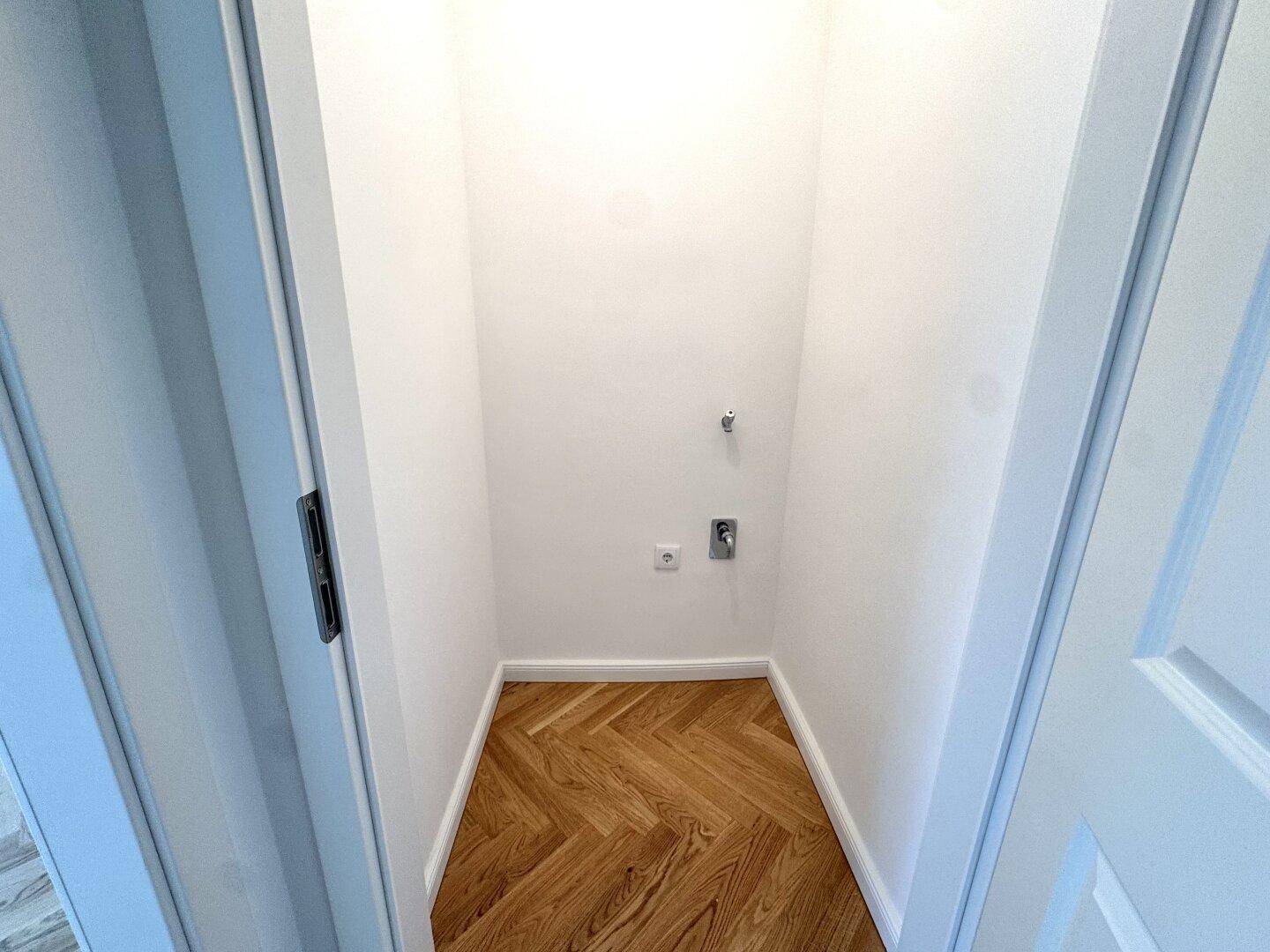 Kleiner Abstellraum mit Parkettboden und Anschlüssen, ideal für Waschmaschine oder Lagerung.