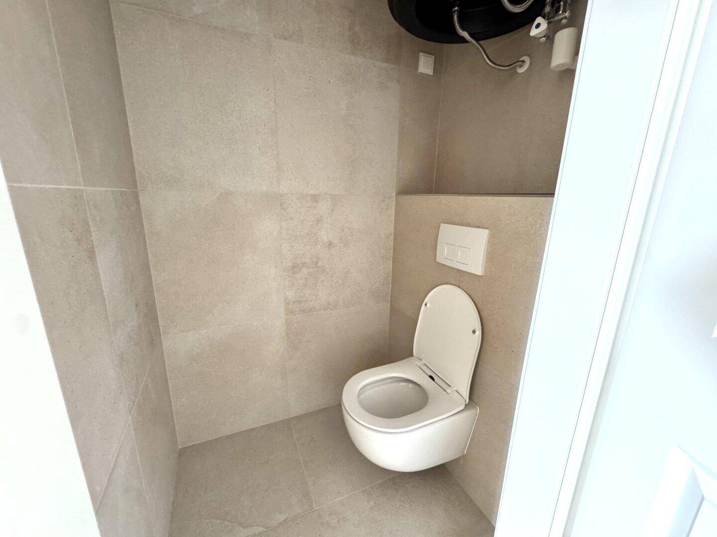 Separates WC mit wandhängender Toilette und modernen, hellen Fliesen.