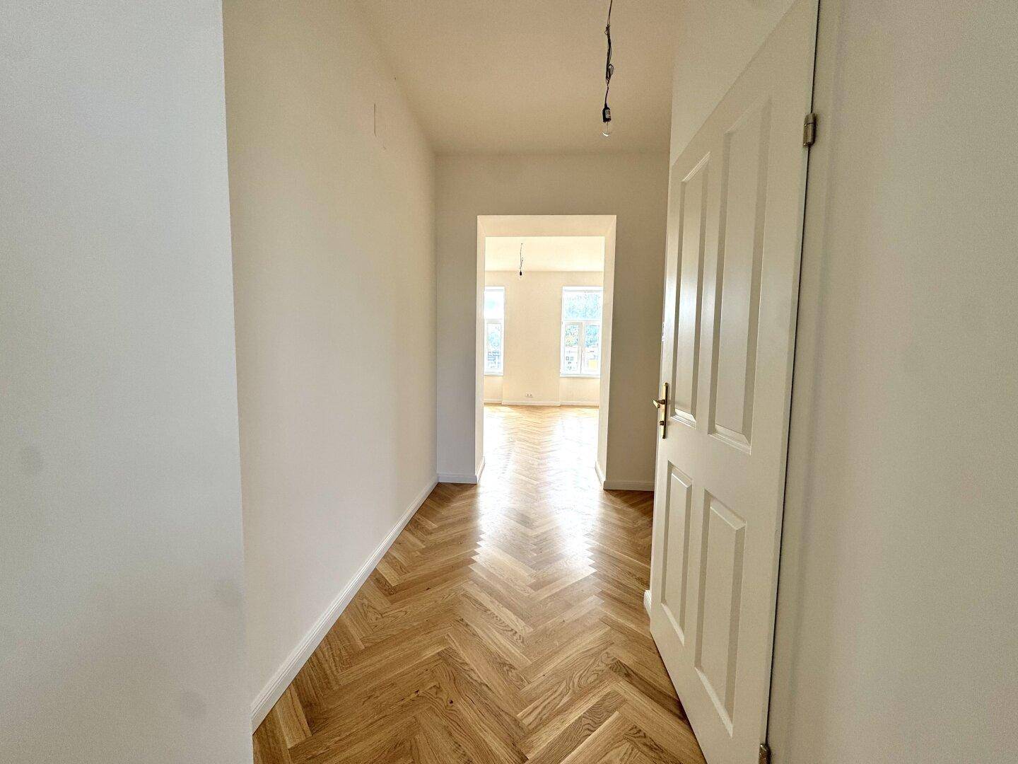 Heller Flur mit Fischgrätparkett, der zu weiteren Zimmern der Wohnung führt.