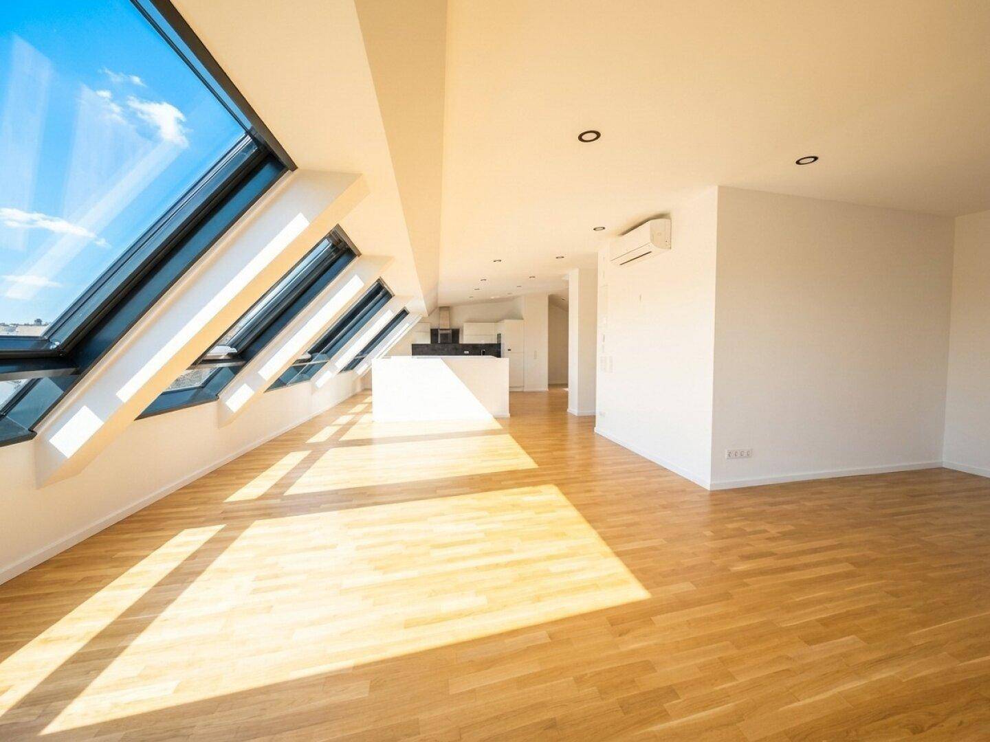 Offener Wohnbereich mit Holzboden, schrägen Dachfenstern und angrenzender Küche, ideal für modernes Wohnen.