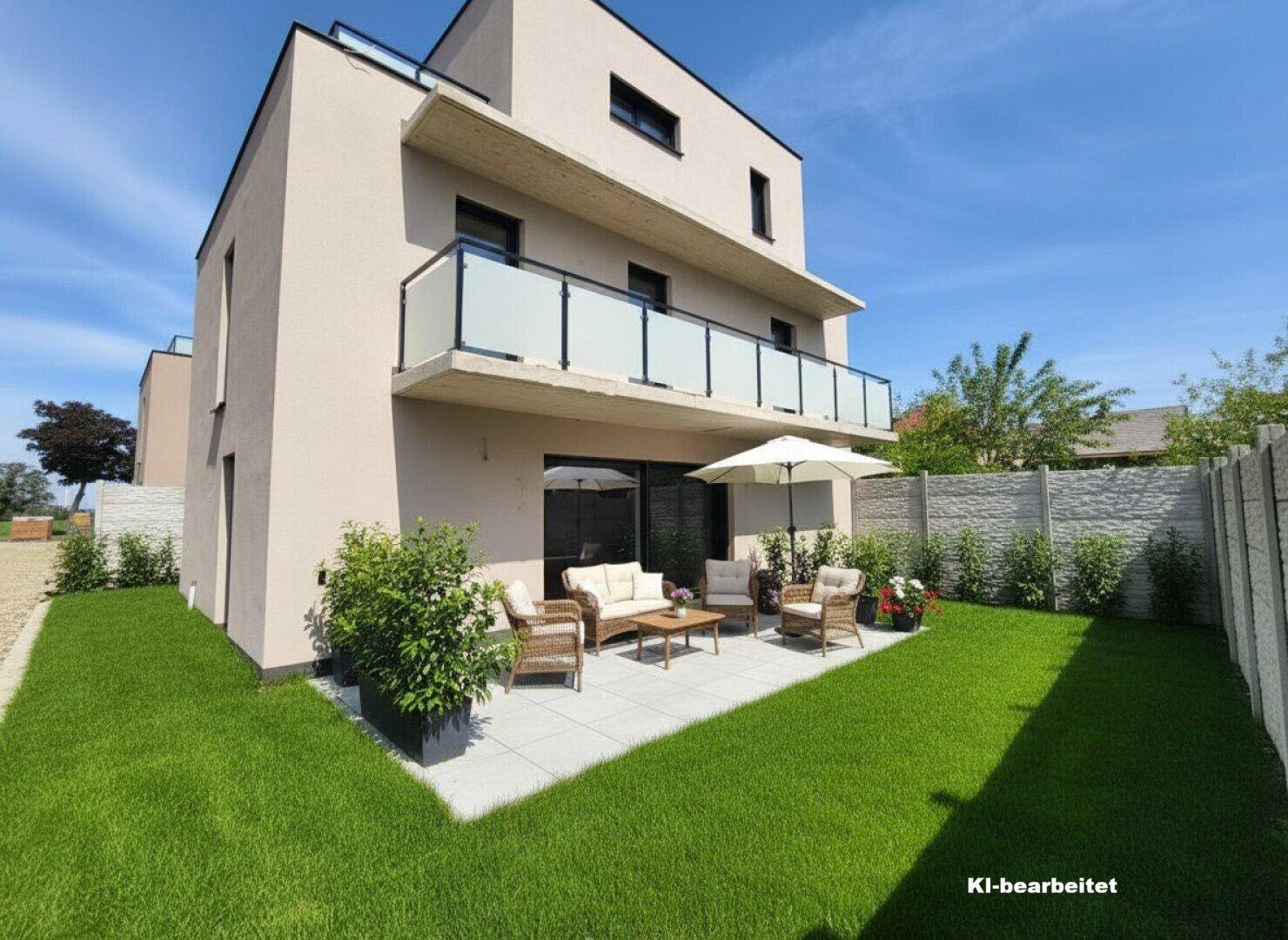 Sonniger Terrassenbereich mit Gartenmöbeln und Rasenfläche neben dem modernen Gebäude.