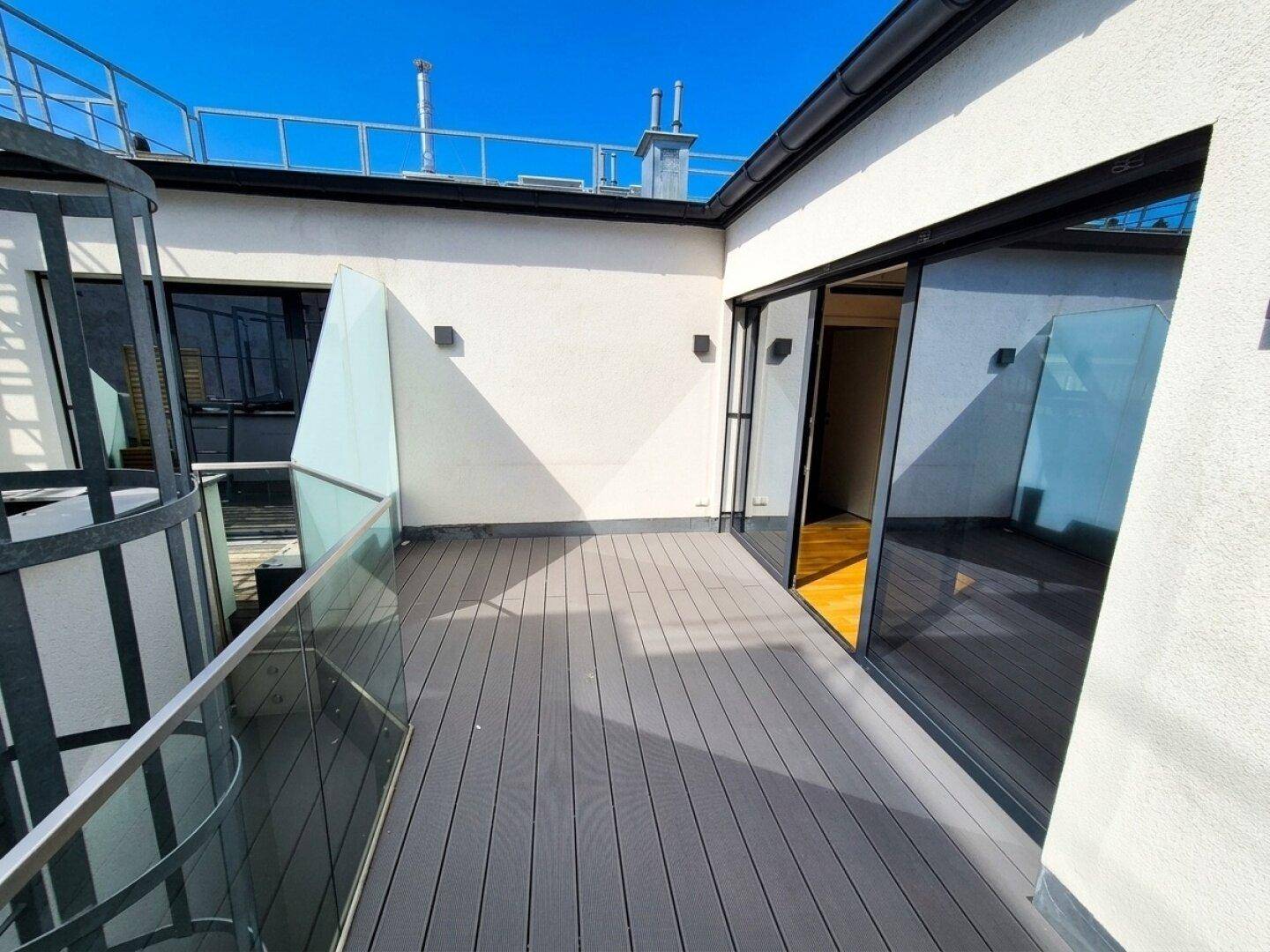 Moderne Dachterrasse mit Holzdielenboden und Glasgeländer, ideal für entspannte Stunden im Freien.