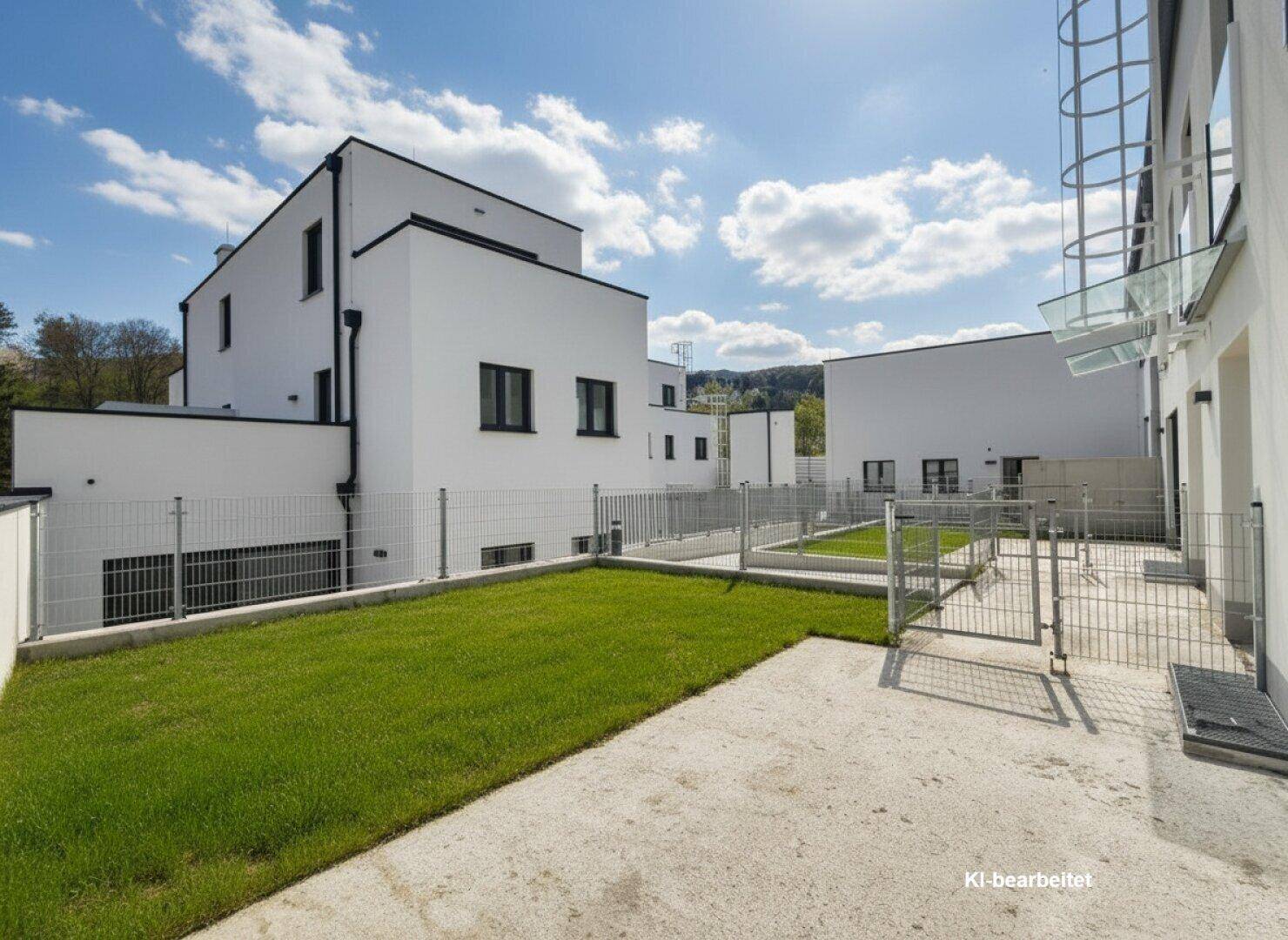 Außenansicht einer modernen Wohnanlage mit umzäuntem Gartenbereich unter blauem Himmel.