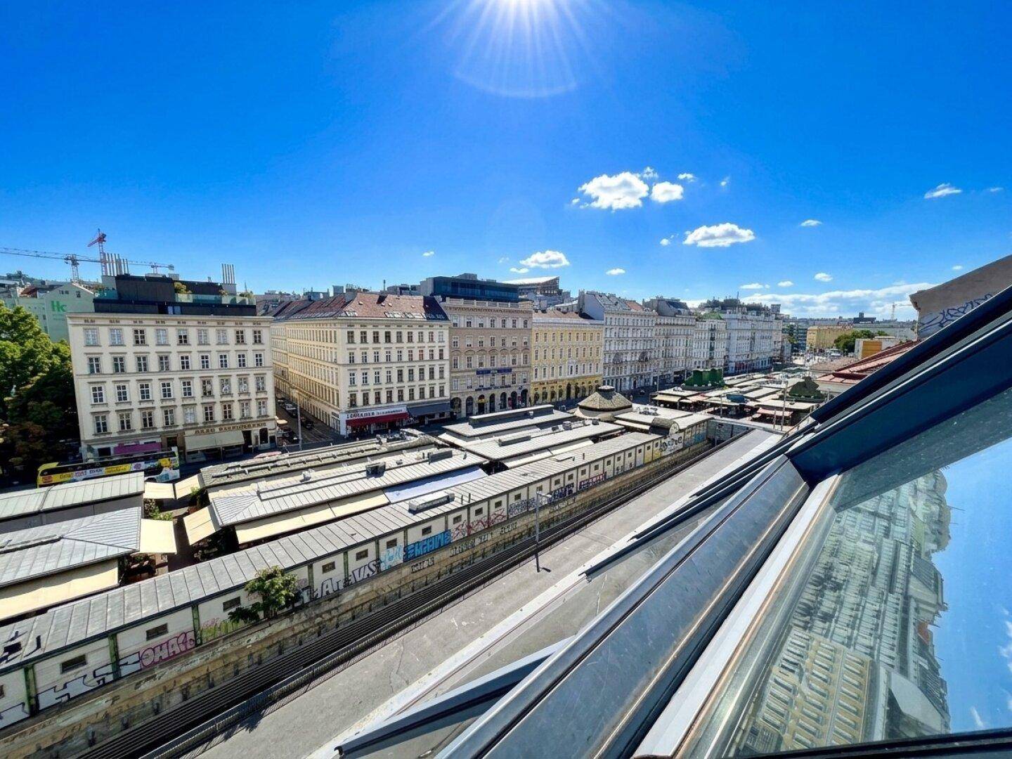Panoramablick über die Stadt mit historischen Gebäuden und einem belebten Marktbereich unter blauem Himmel.