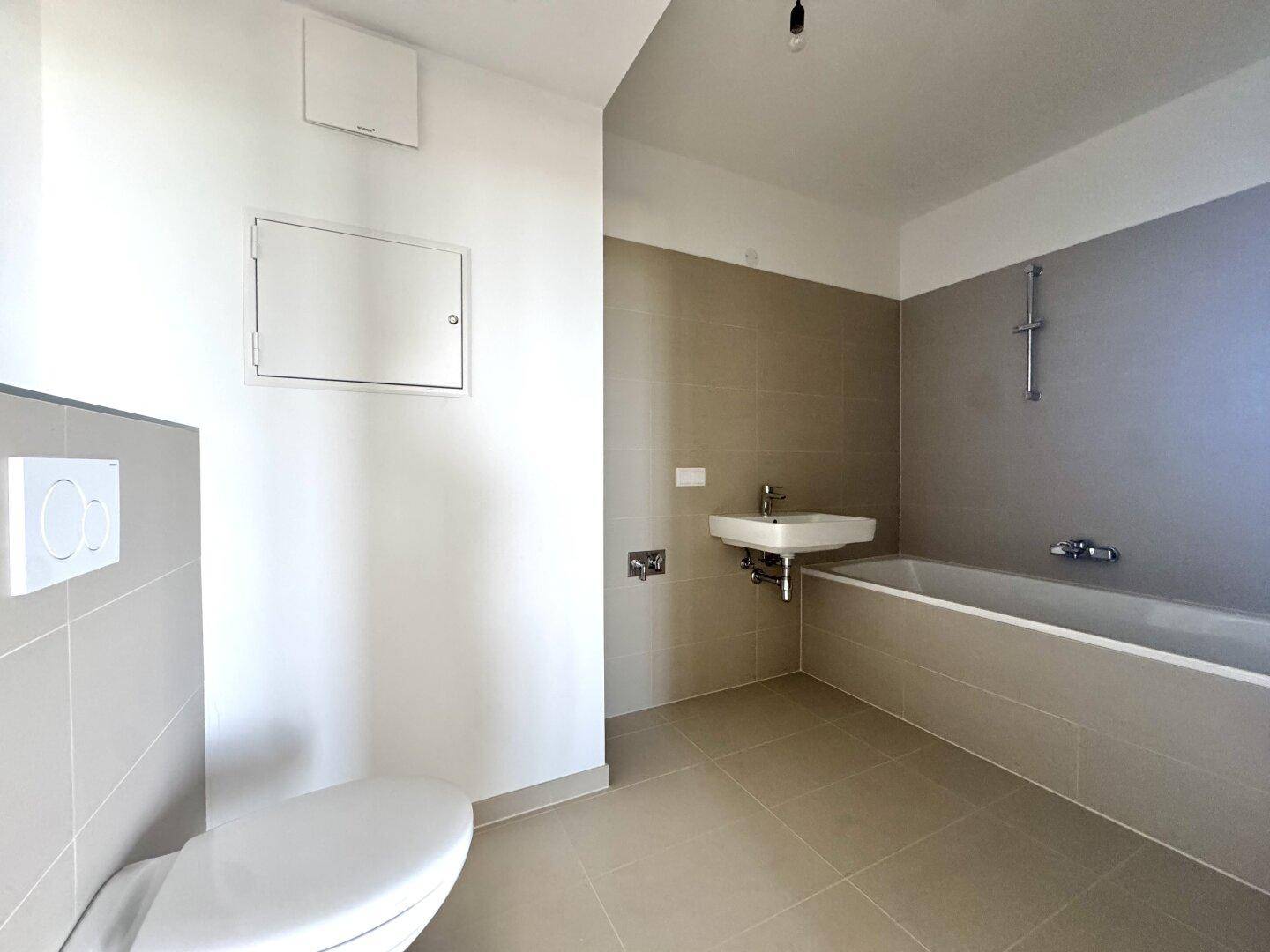 Modernes Badezimmer mit Badewanne, Toilette und Waschbecken, in neutralen Grautönen gefliest.