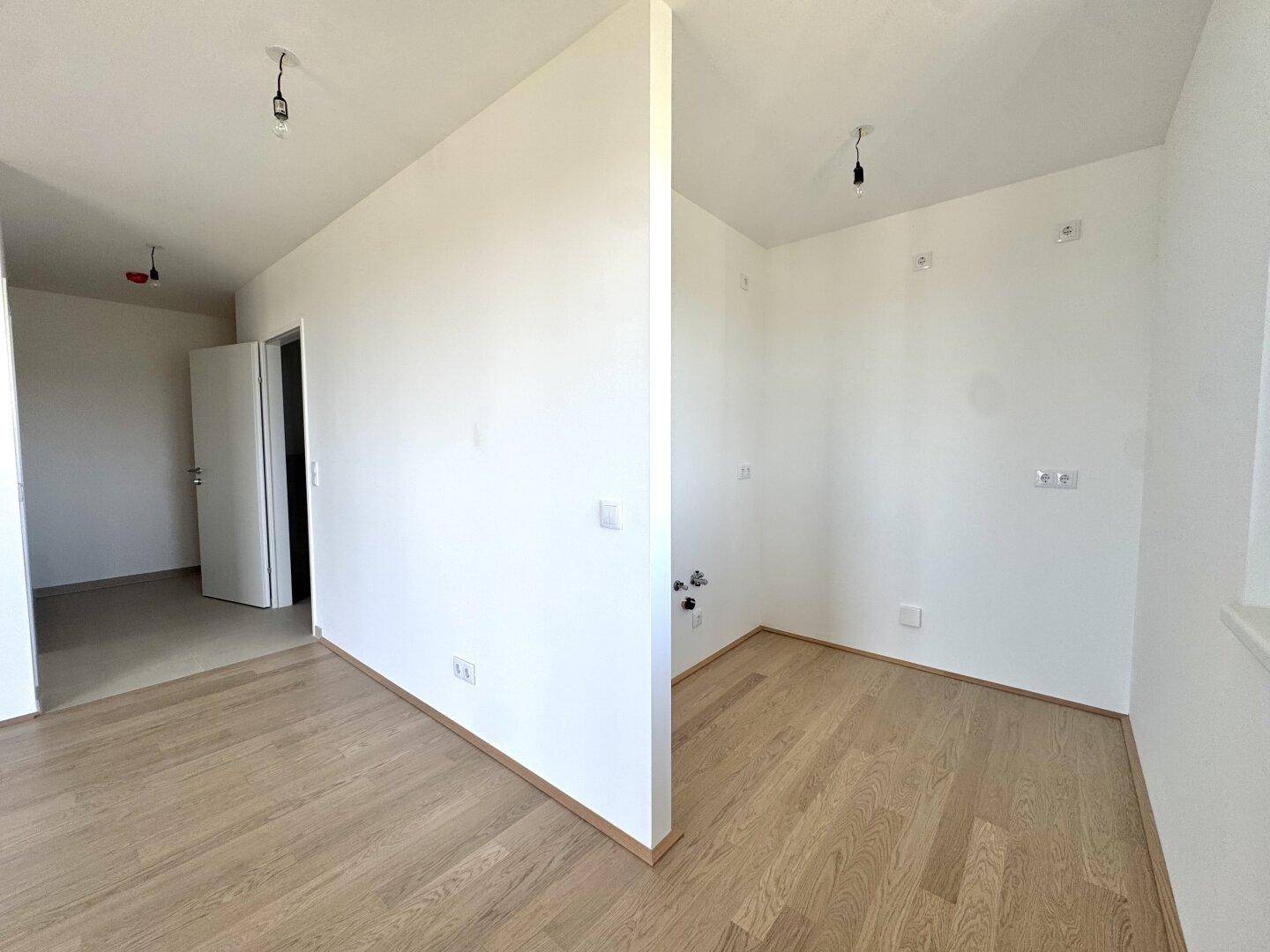 Leerer Raum mit Anschlüssen für eine Küche oder einen Hauswirtschaftsraum, mit Holzboden.