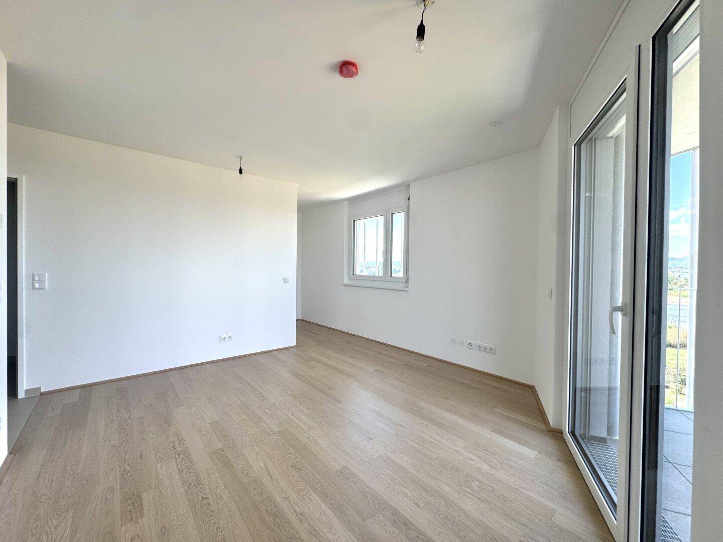 Helles, leeres Wohnzimmer mit Holzboden und großen Fenstern, bereit zur individuellen Gestaltung.