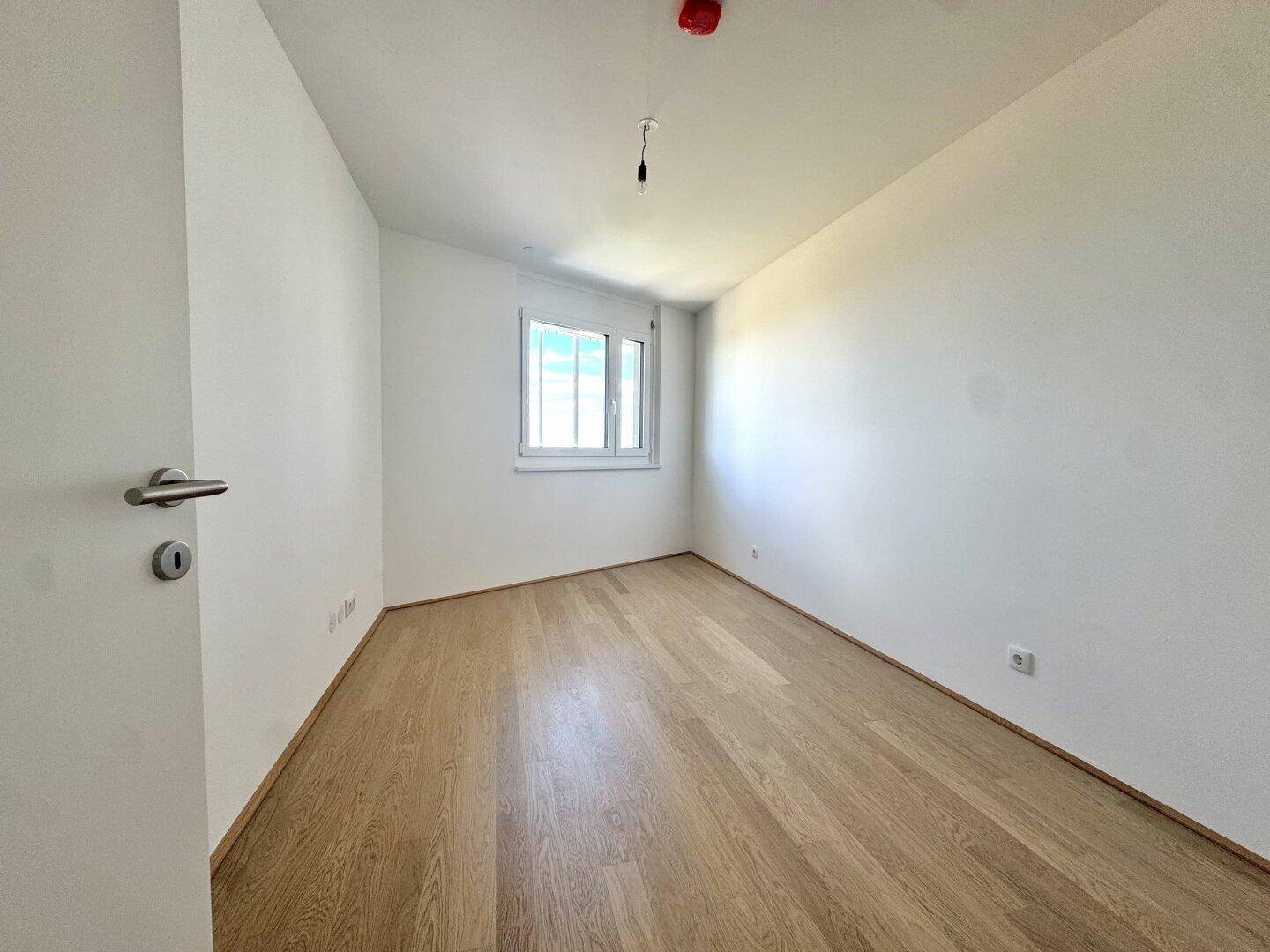 Helles, leeres Schlafzimmer mit Holzboden und einem Fenster, bereit zur Einrichtung.