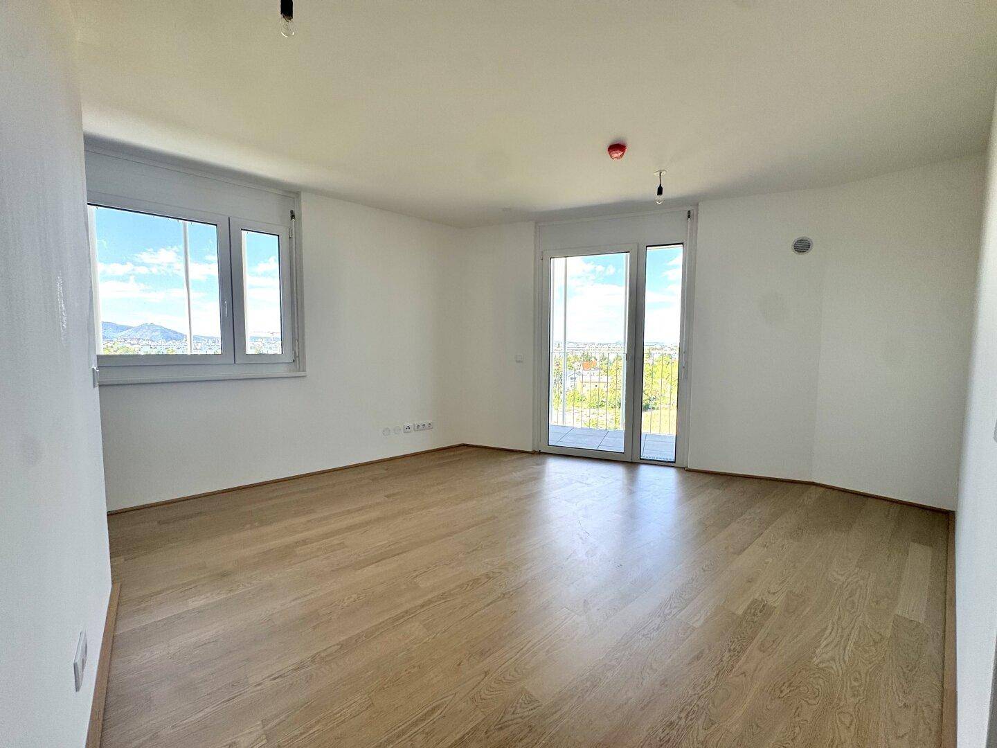 Heller, leerer Raum mit Holzboden und Zugang zu einem französischen Balkon oder einer kleinen Terrasse.