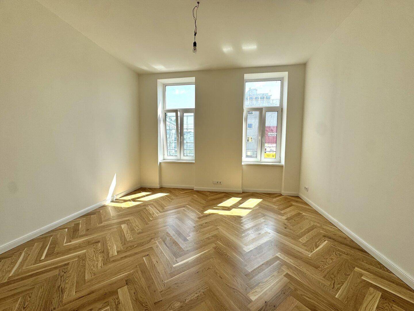 Gemütlicher Raum mit Fischgrätparkett und zwei Fenstern, die für angenehmes Tageslicht sorgen.