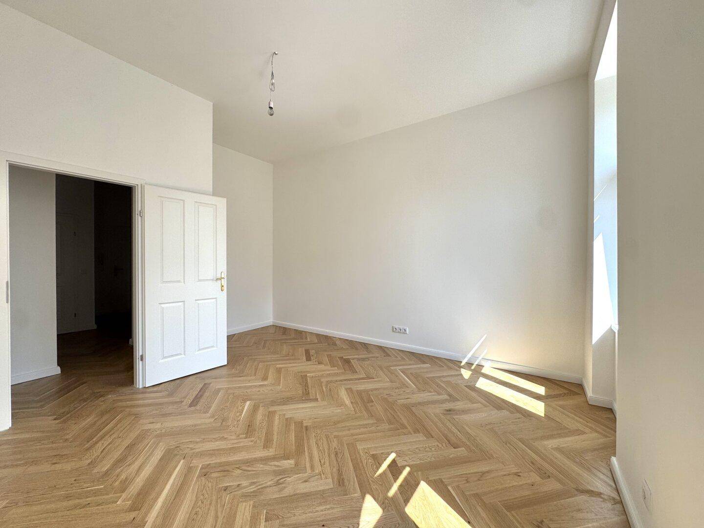 Geräumiges Zimmer mit Fischgrätparkett, Bogenfenster und Zugang zu weiteren Räumen.