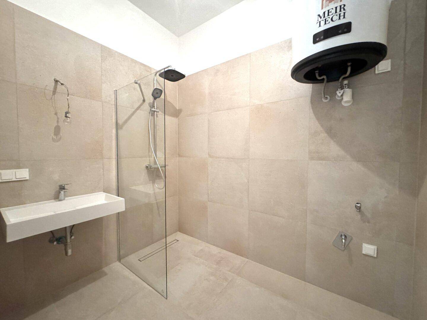 Modernes Badezimmer mit begehbarer Dusche, Wandwaschbecken und beigefarbenen Fliesen.