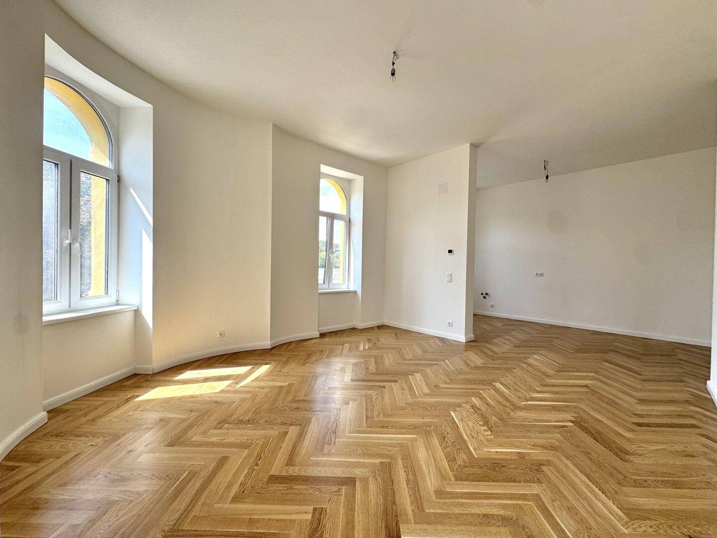Lichtdurchfluteter Raum mit elegantem Fischgrätparkett und charakteristischen Bogenfenstern.