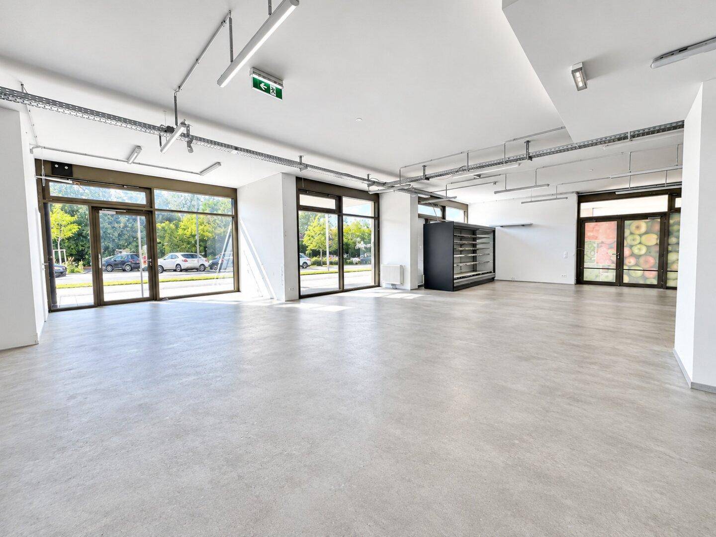 Geräumiger, leerer Geschäftsraum mit großen Schaufenstern und Betonboden, ideal für Einzelhandel.