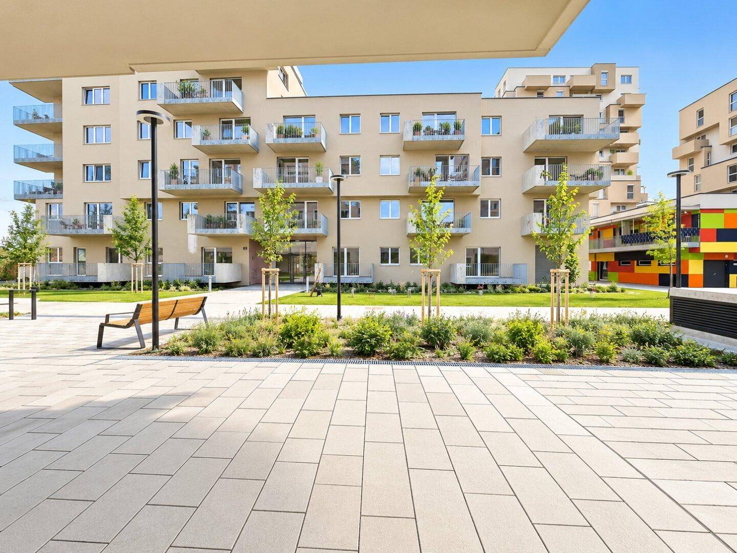 Ansicht eines modernen Wohngebäudes mit vielen Balkonen und einem gepflegten Innenhof mit Bänken.