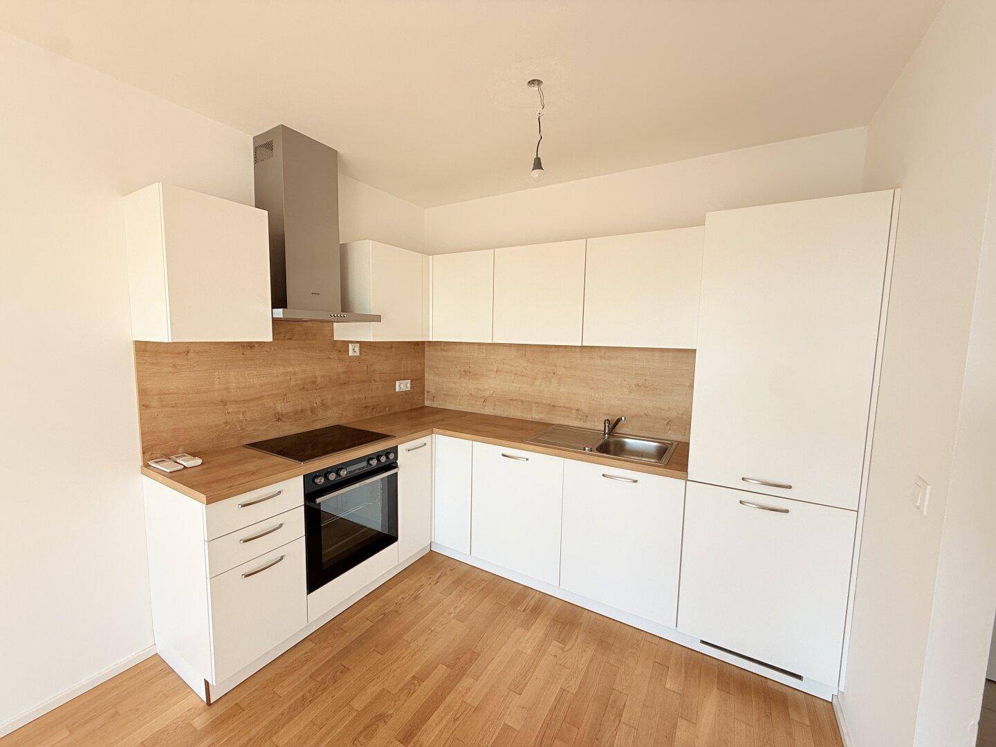 Gut ausgestattete Küche mit weißen Fronten, Holzdetails und modernen Kochgeräten.