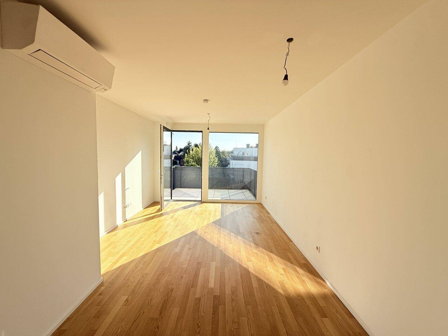 Lichtdurchfluteter Wohnbereich mit Zugang zum Balkon und Holzboden, ideal für entspannte Stunden.