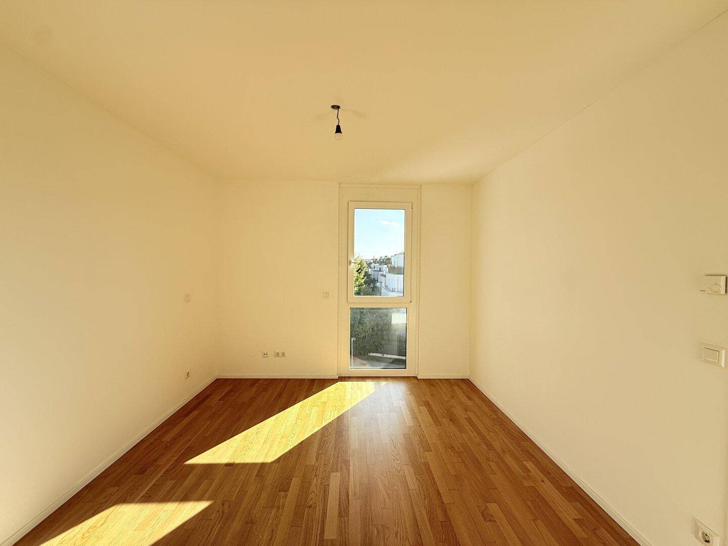 Lichtdurchflutetes Schlafzimmer mit großem Fenster und Holzboden, bietet eine angenehme Atmosphäre.
