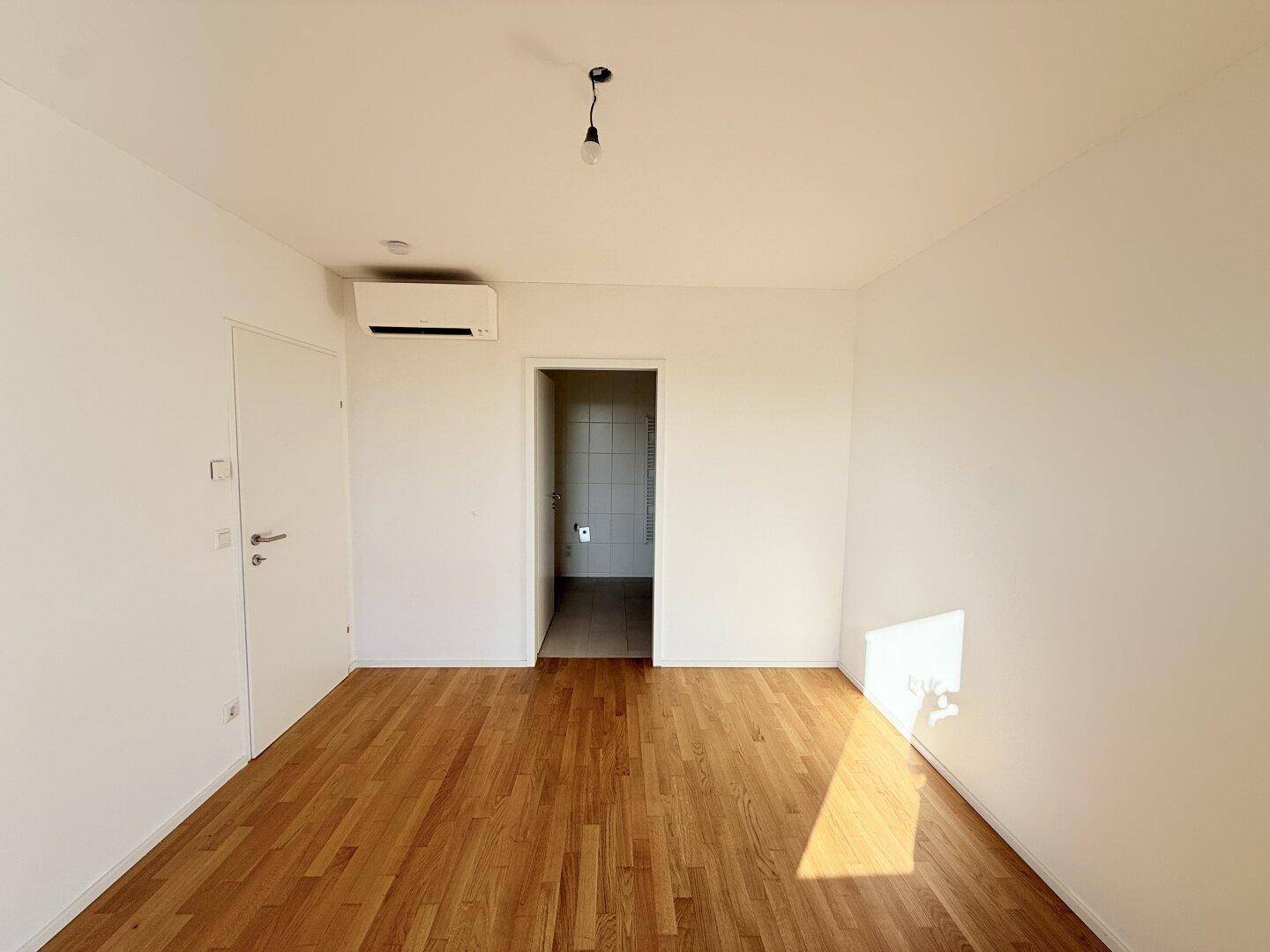 Schlafzimmer mit Holzboden, Klimaanlage und Zugang zum Badezimmer, ideal für Komfort.