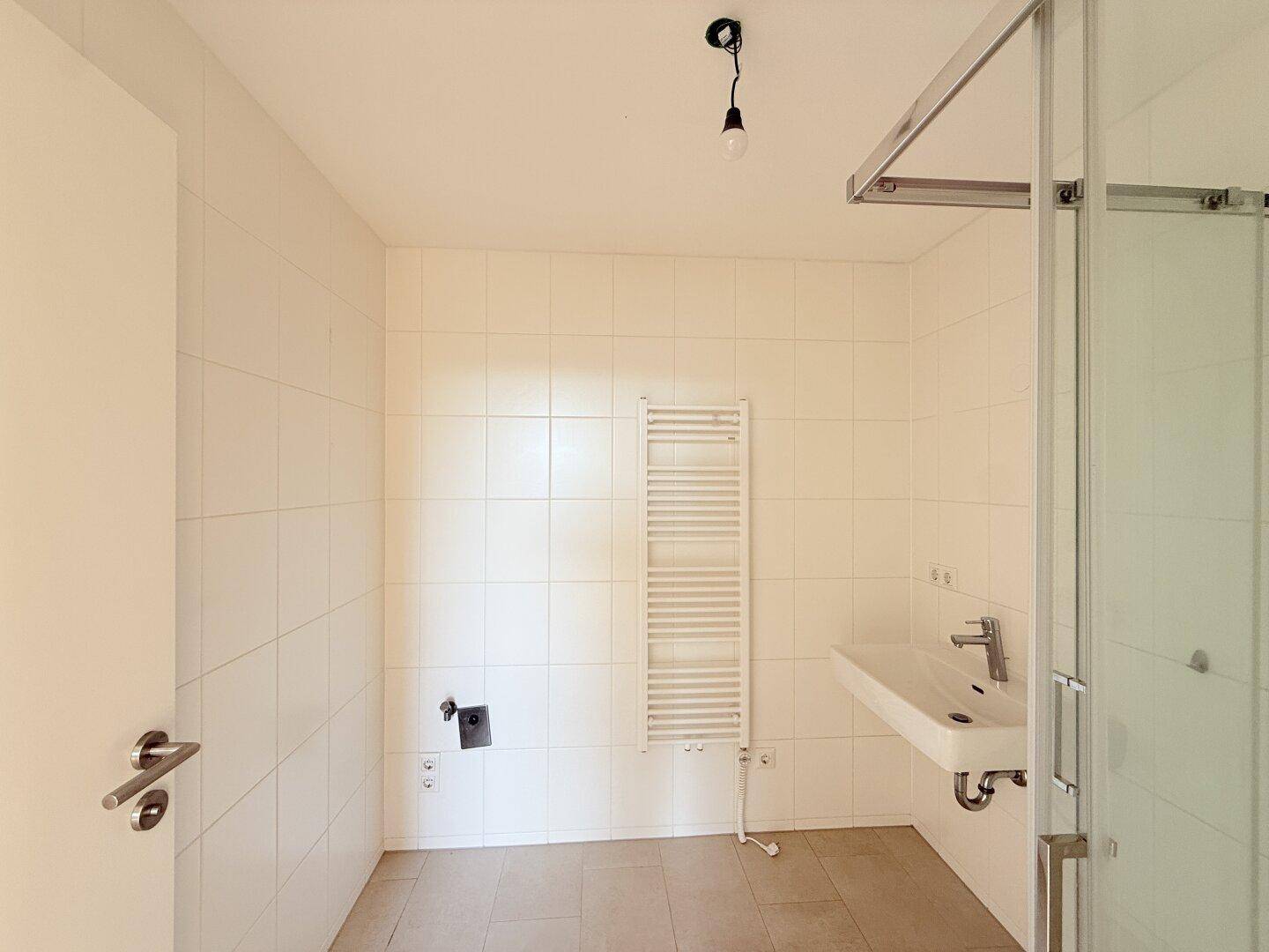 Modernes Badezimmer mit weißen Fliesen, Dusche und beheiztem Handtuchhalter.